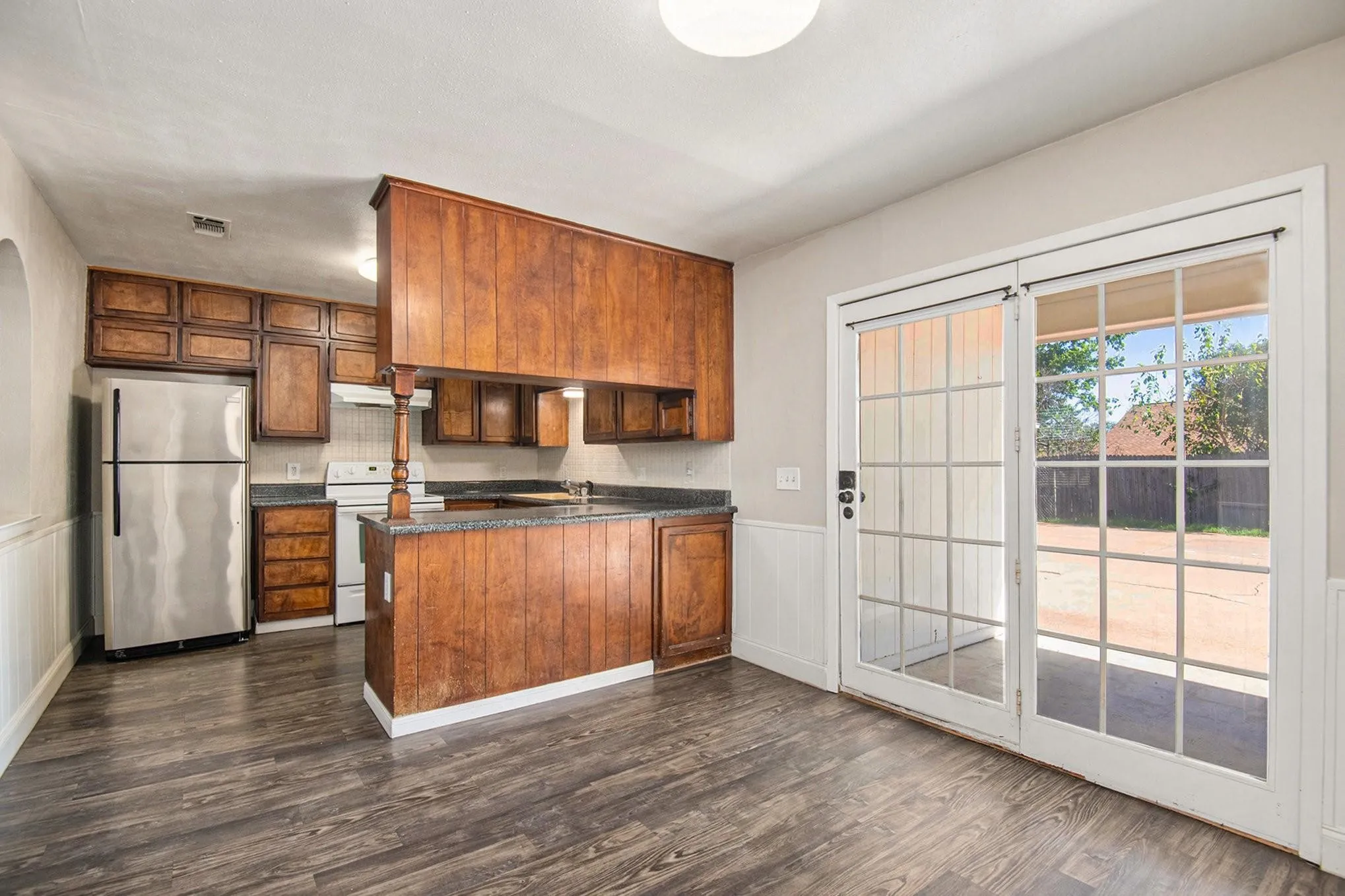 Kitchen and dining area featuring wood-finish flooring, wood cabinetry, stone countertops, and stainless steel appliances