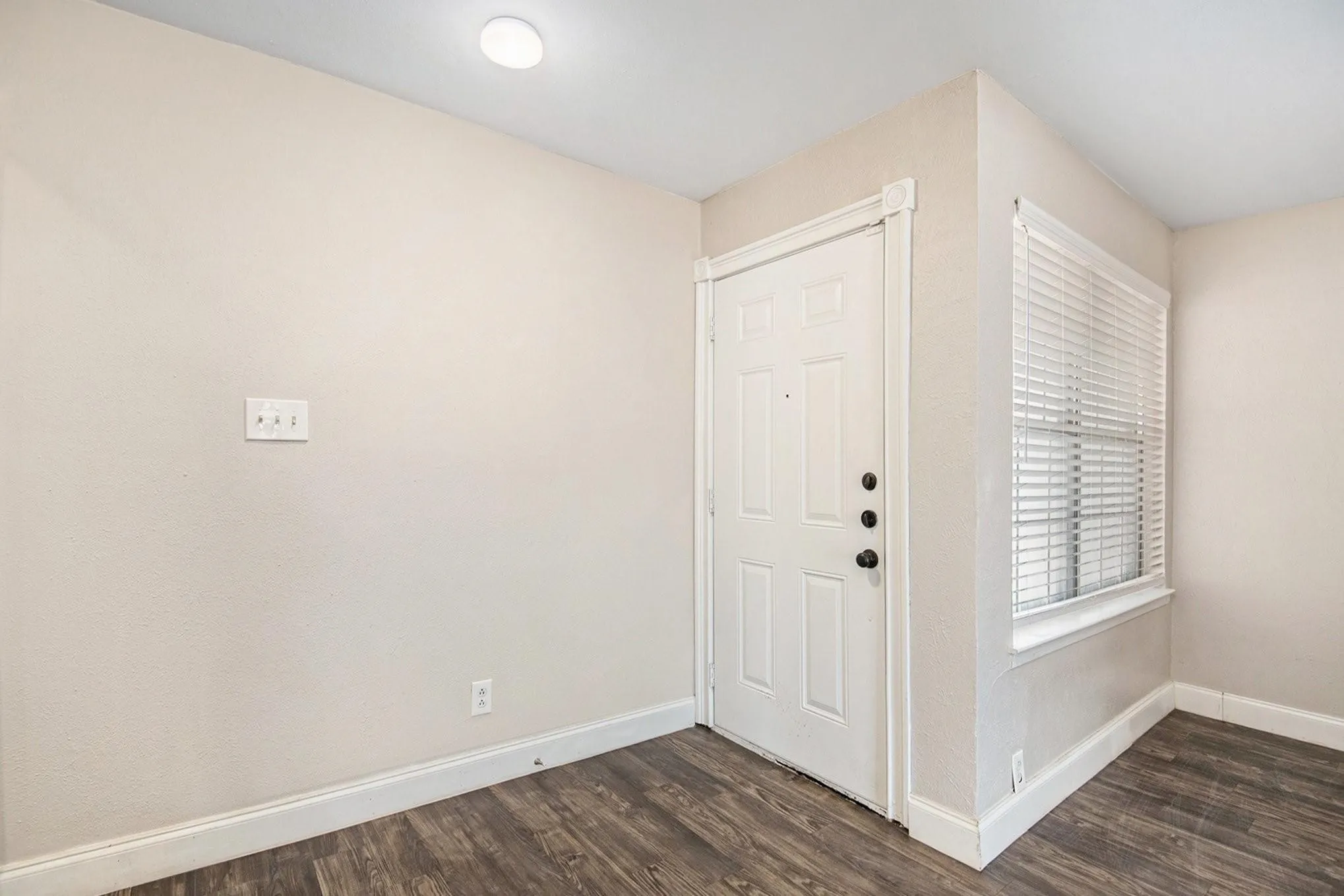 Entryway featuring a paneled door with dark hardware, a window with horizontal blinds, and wood-finish flooring