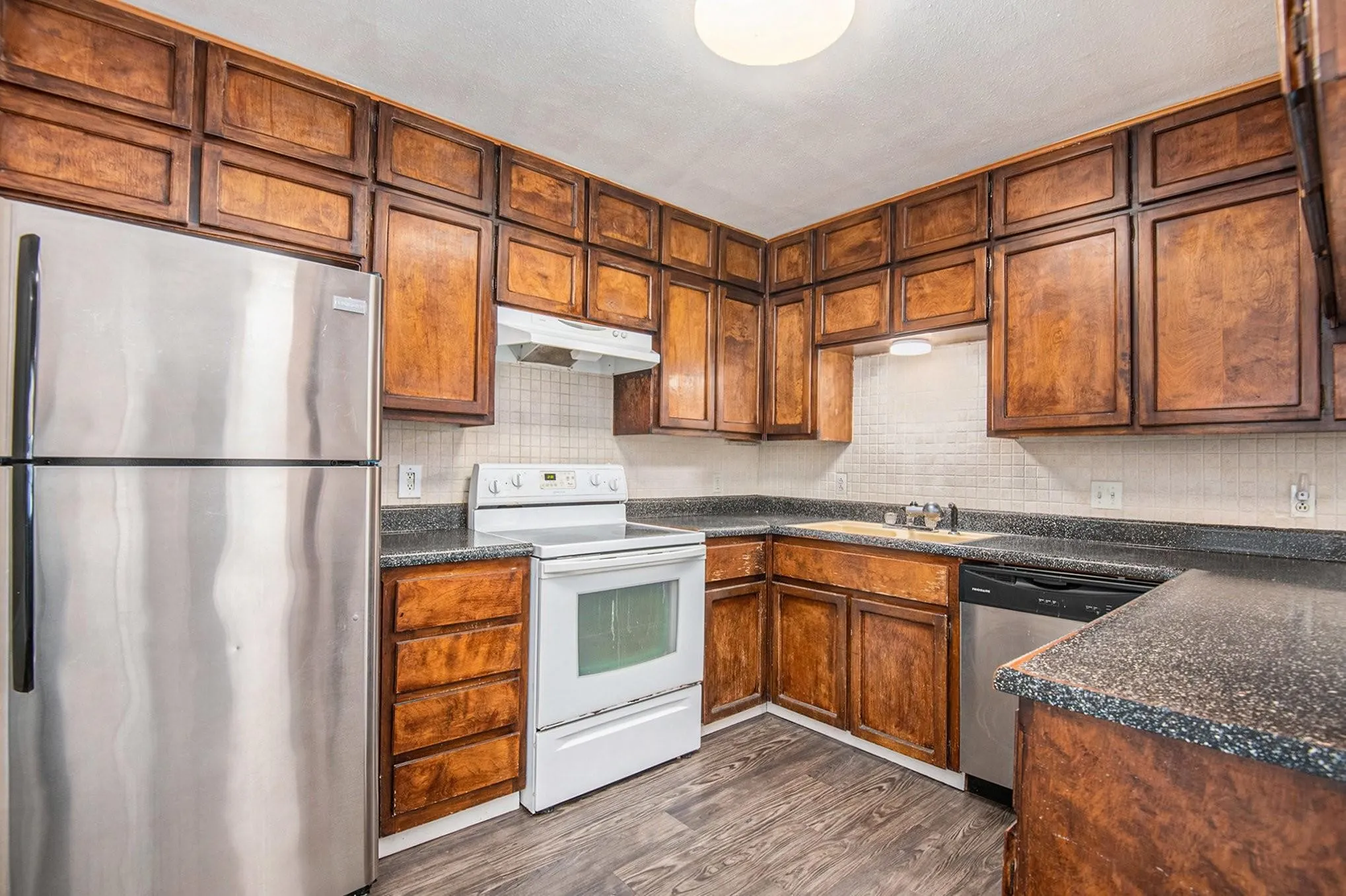 Kitchen featuring abundant wood cabinetry, dark speckled countertops, stainless steel refrigerator and dishwasher, white electric range with matching hood, and wood-finish flooring