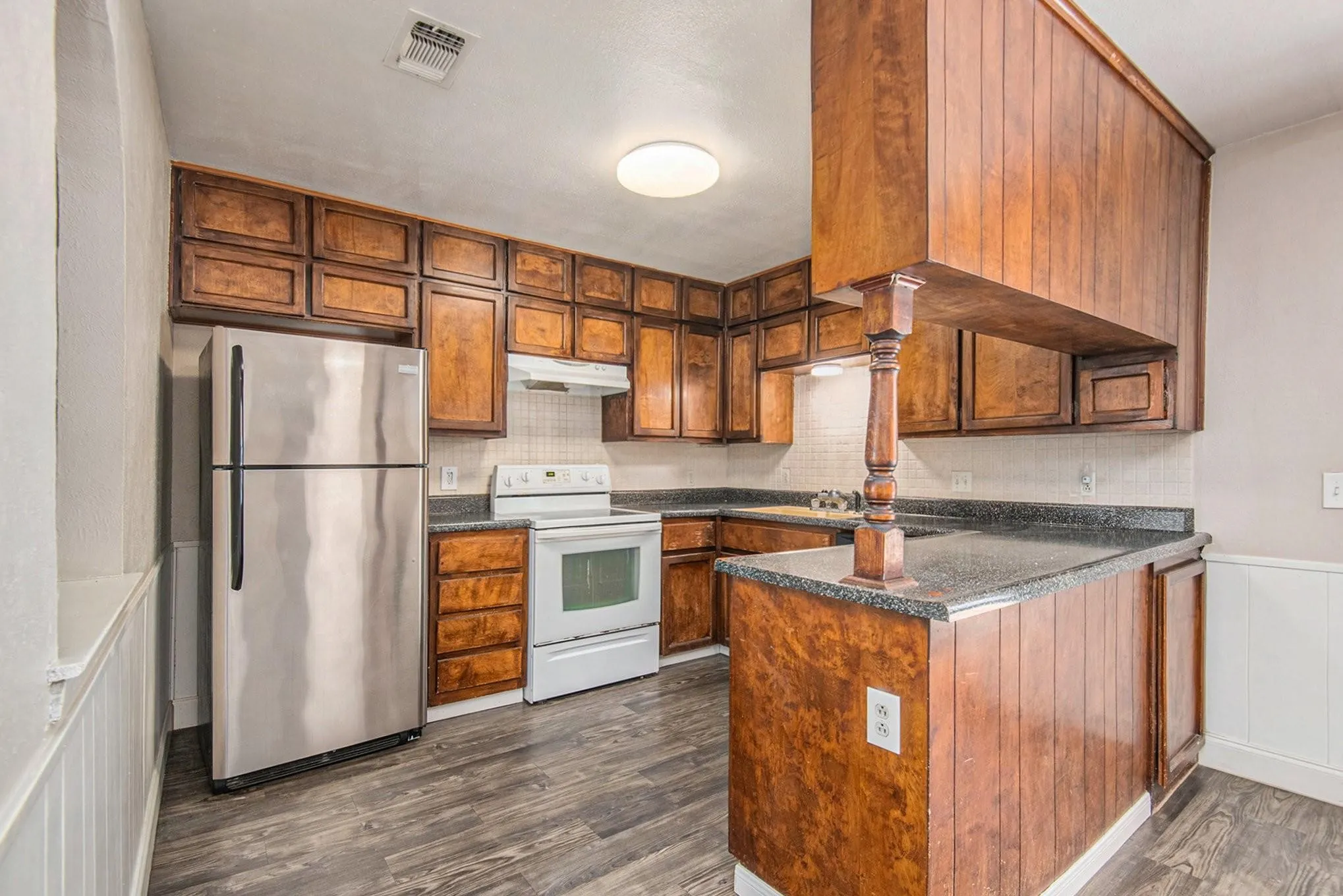 Kitchen featuring dark wood-finish cabinetry, granite-style countertops, white tile backsplash, and wood-finish flooring