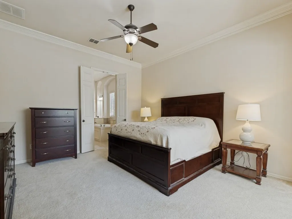 Plush carpeting and crown molding frame this spacious room, featuring a ceiling fan with integrated lighting