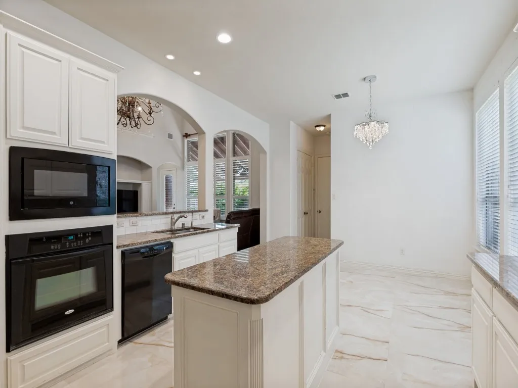 Kitchen featuring white cabinetry, built-in black appliances, a central island with a stone-finish countertop, and a crystal​​‌​​​​‌​​‌‌​‌‌​​​‌‌​‌​‌​‌​​​‌​​ chandelier