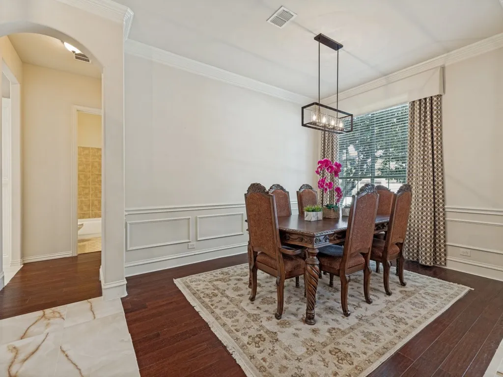 Dining area featuring dark wood-finish flooring, wainscoting, crown molding, and a modern rectangular chandelier