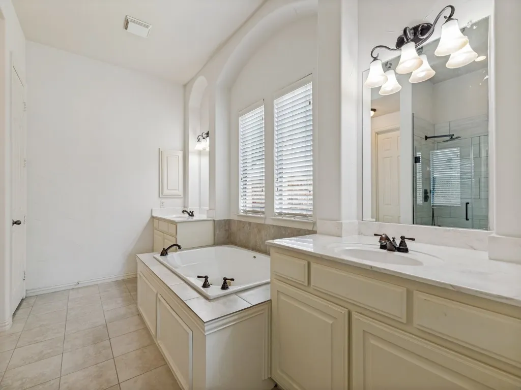 Spacious bathroom featuring a built-in tub with tile surround, dual vanity with undermount sinks, and a framed mirror with an overhead light fixture