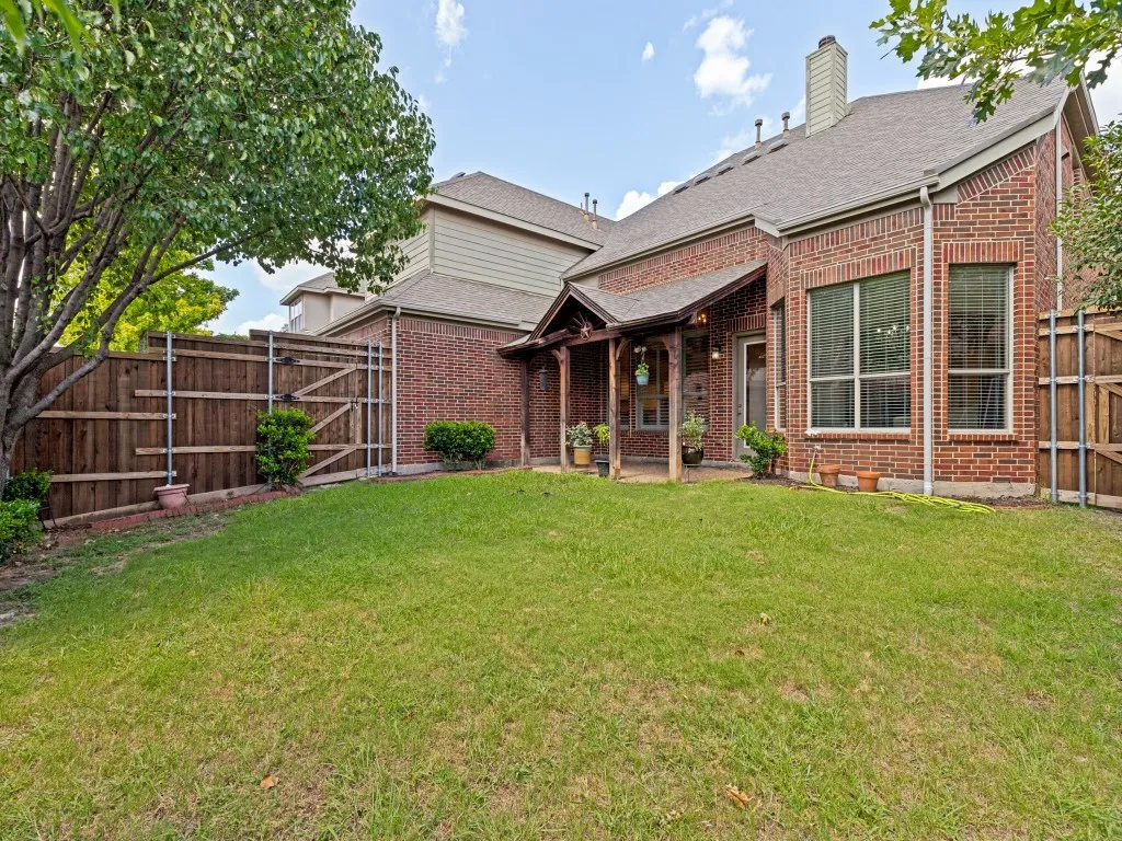 Expansive green lawn with a covered patio area, brick exterior, fenced perimeter, and mature tree