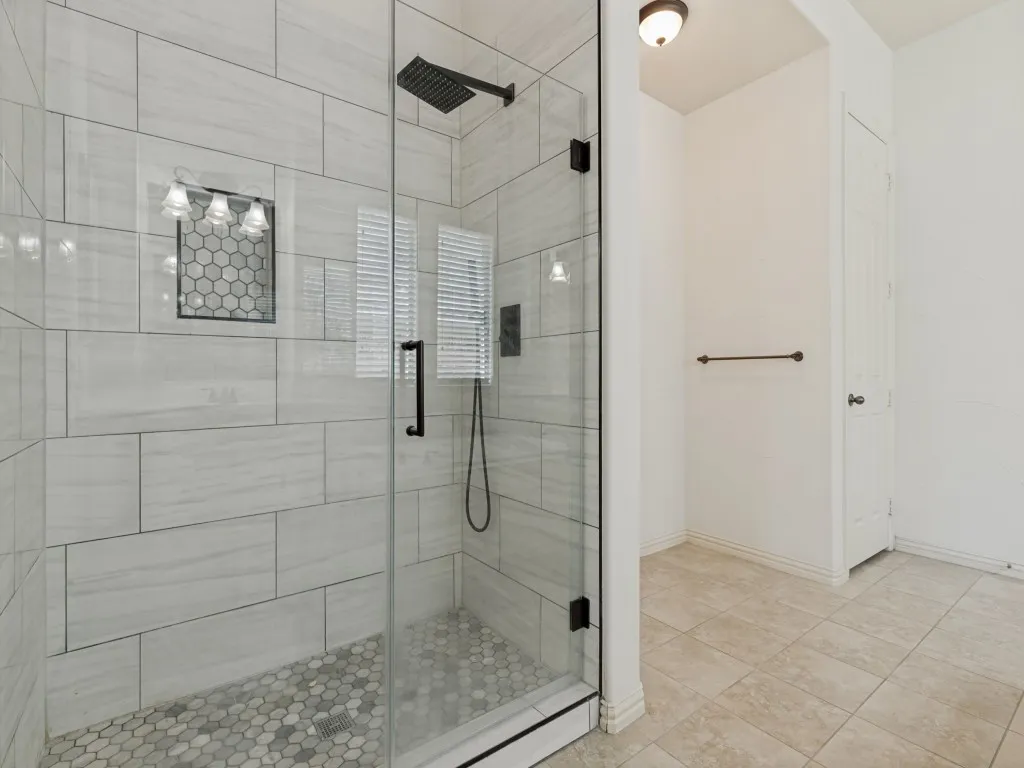 Walk-in shower featuring a frameless glass enclosure, a matte black showerhead, and light-toned rectangular wall tiles