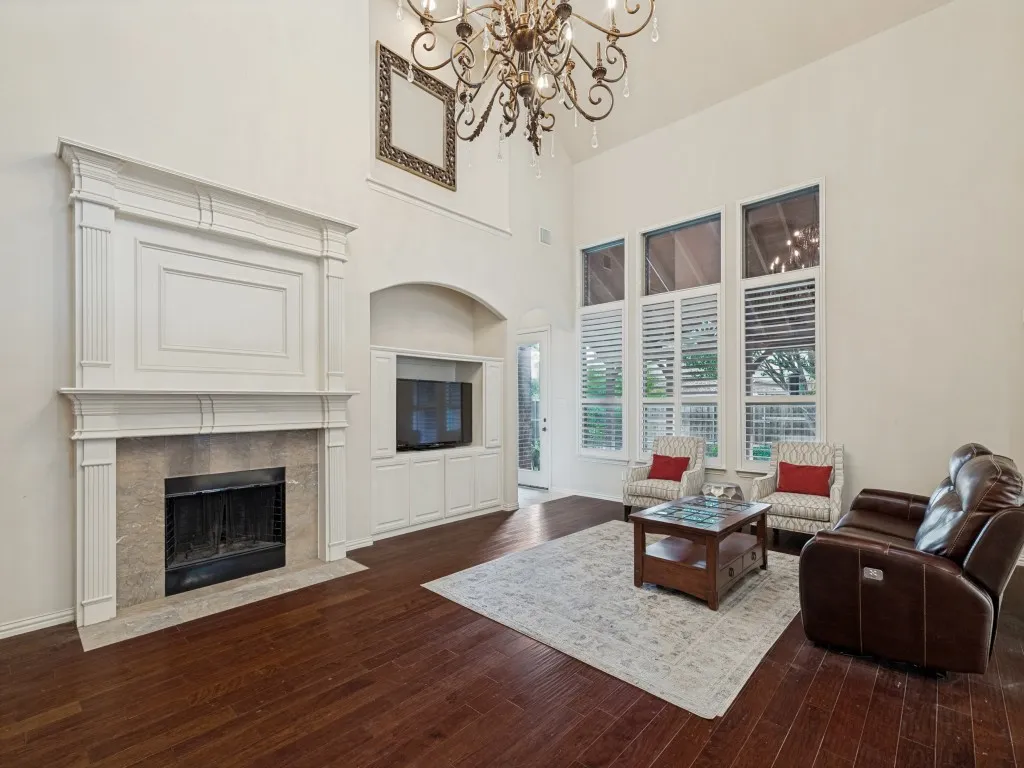 Vaulted ceiling living room featuring a grand fireplace with a stone surround, built-in media cabinetry, wood-finish flooring, and a large chandelier
