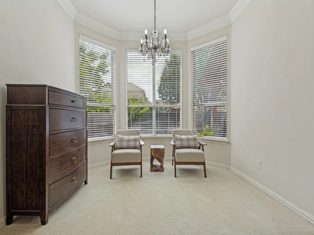 Bay window configuration providing abundant natural light, crown molding detailing, and a prominent chandelier