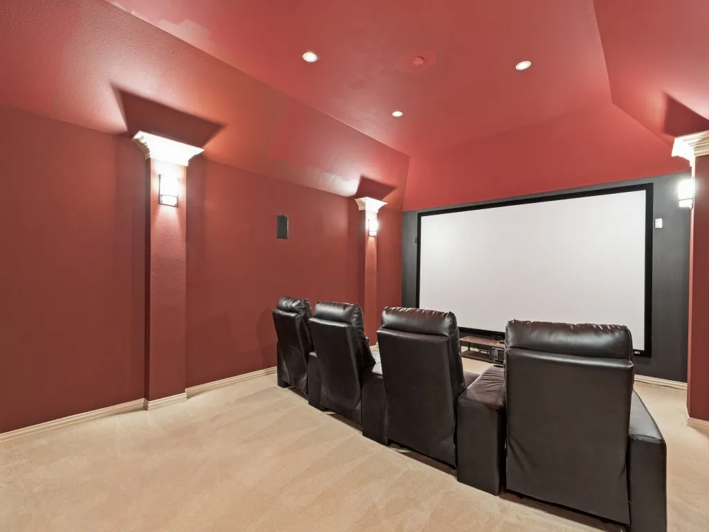Dedicated media room featuring a large projection screen, recessed ceiling lighting, and wall sconces
