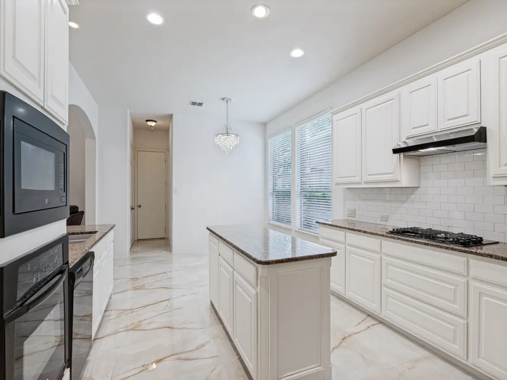 Bright kitchen featuring an island, granite countertops, tile backsplash, white cabinetry, and large windows