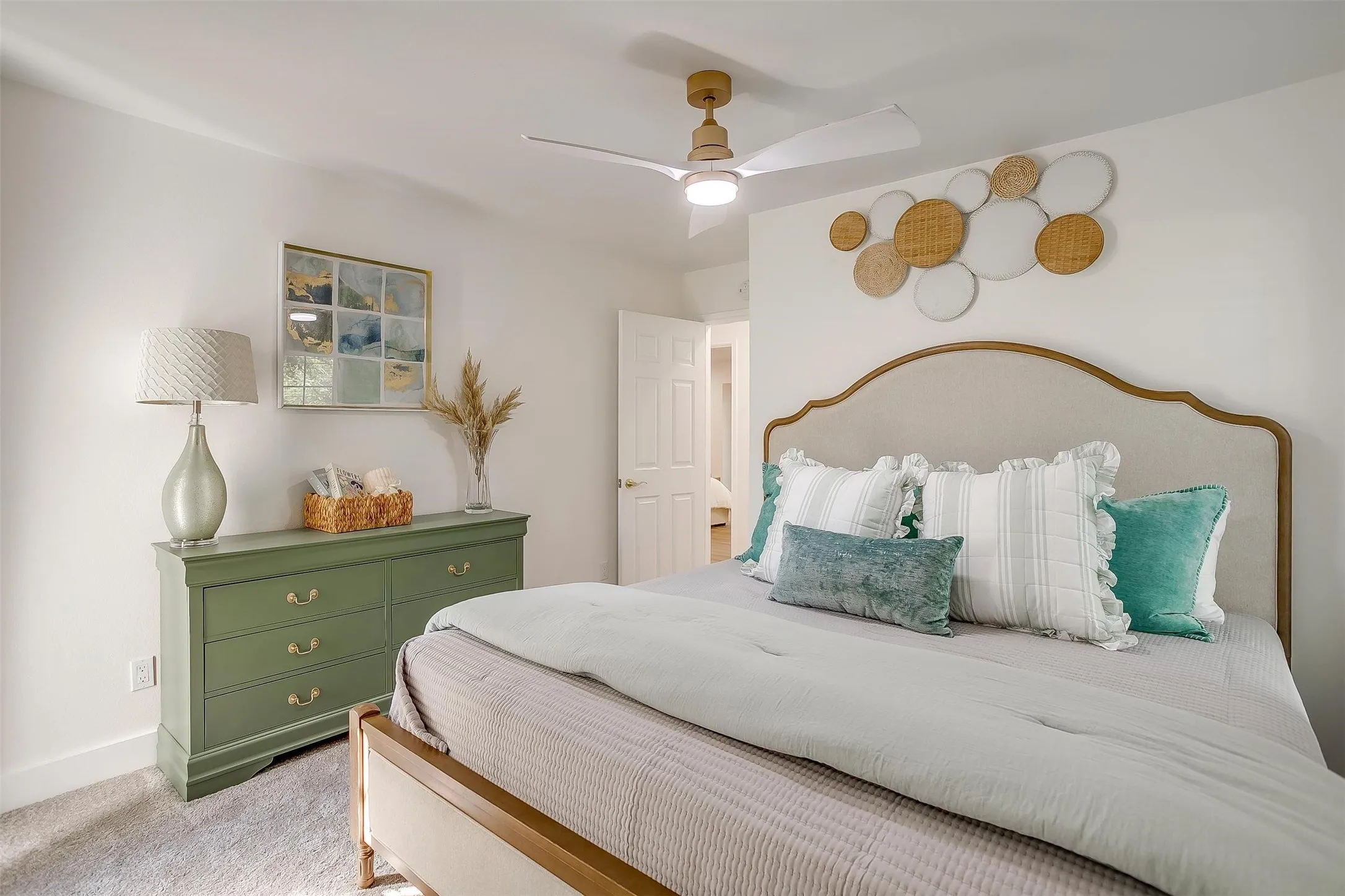 Bright bedroom with light-colored carpeting, white walls, a ceiling fan with a light fixture, and an arched upholstered headboard