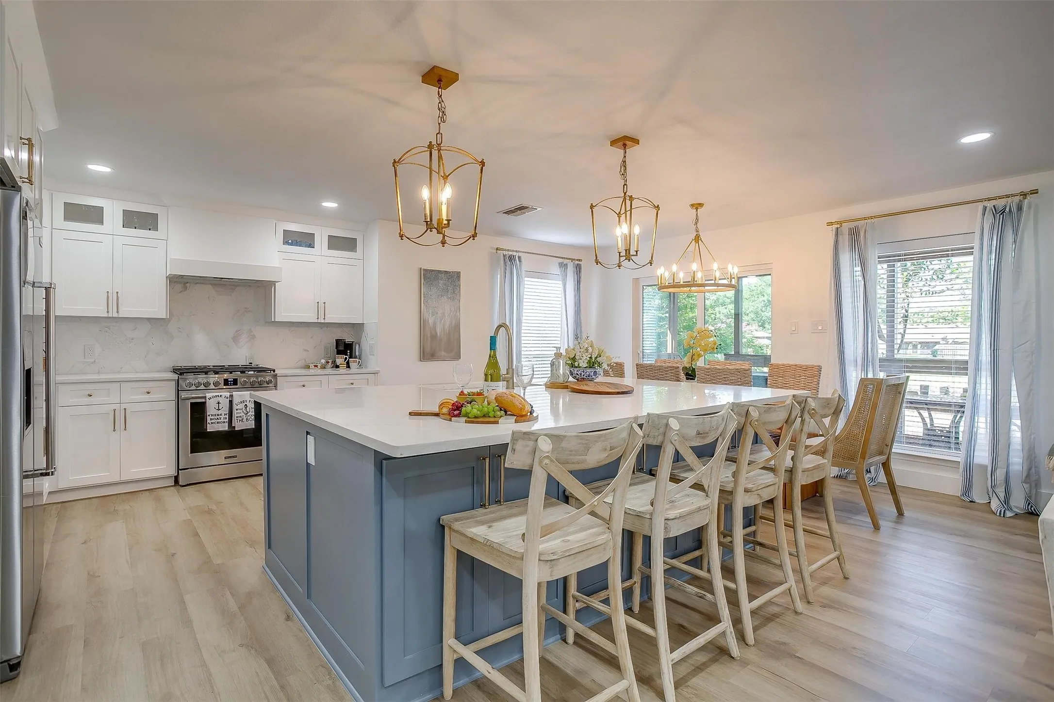Spacious kitchen featuring a large island with seating, stainless steel appliances, wood-finish flooring, white cabinetry, and recessed lighting