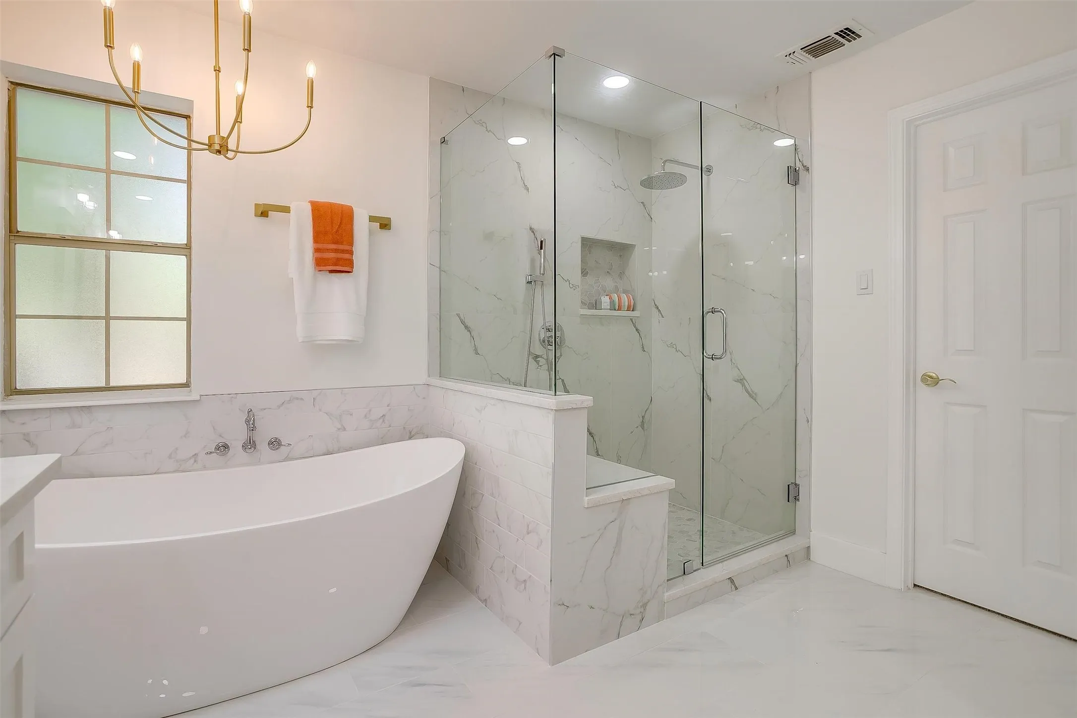 Contemporary bathroom featuring a freestanding soaking tub, a frameless glass shower enclosure with a built-in bench, and white marble-look tile flooring