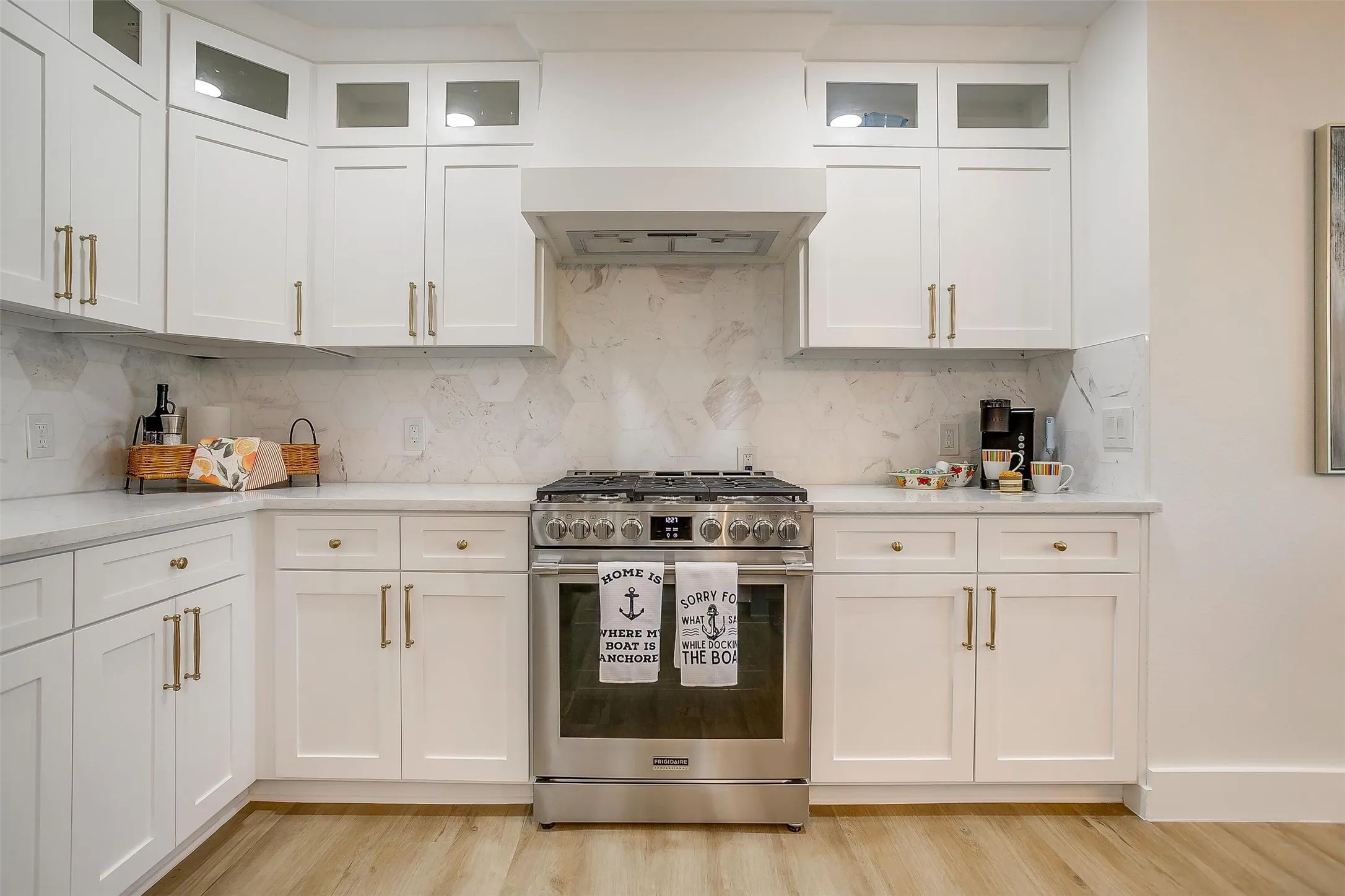 Contemporary kitchen with white shaker cabinetry, gold-tone hardware, and light-toned countertops
