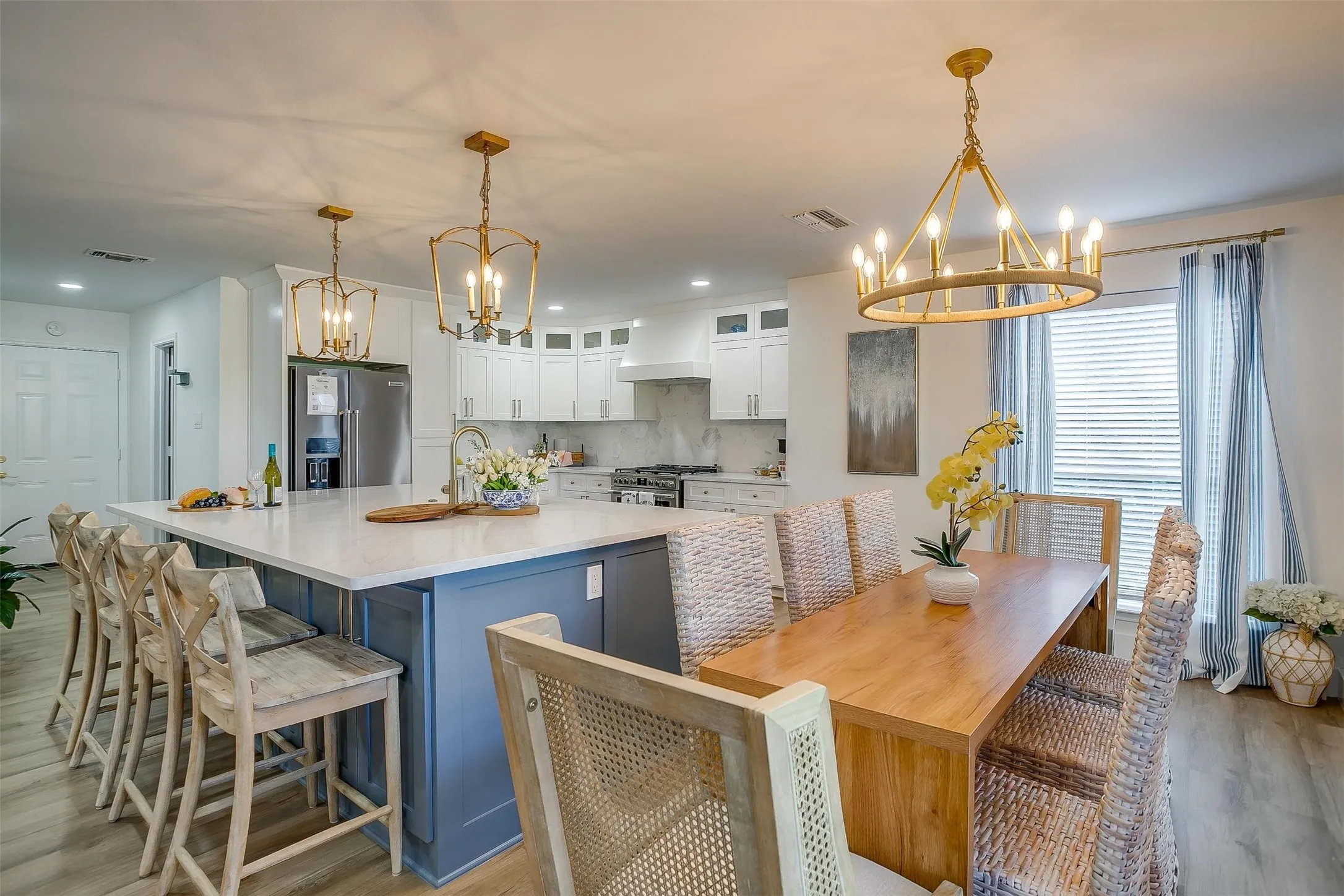 Spacious kitchen featuring a large central island with seating, stone countertops, white cabinetry, integrated stainless steel appliances, and wood-finish flooring