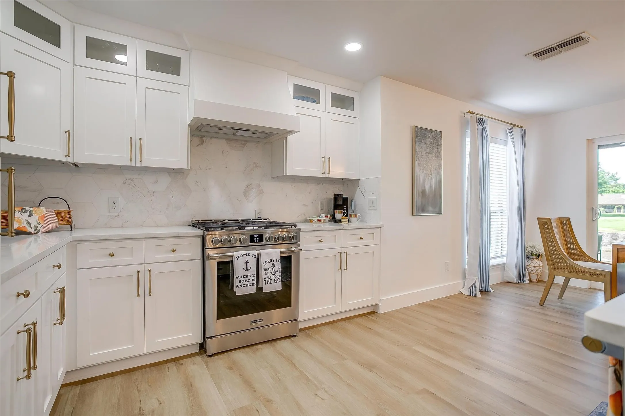 Modern kitchen featuring white shaker cabinetry with gold-finish hardware, stainless steel range, and light-toned wood-finish flooring