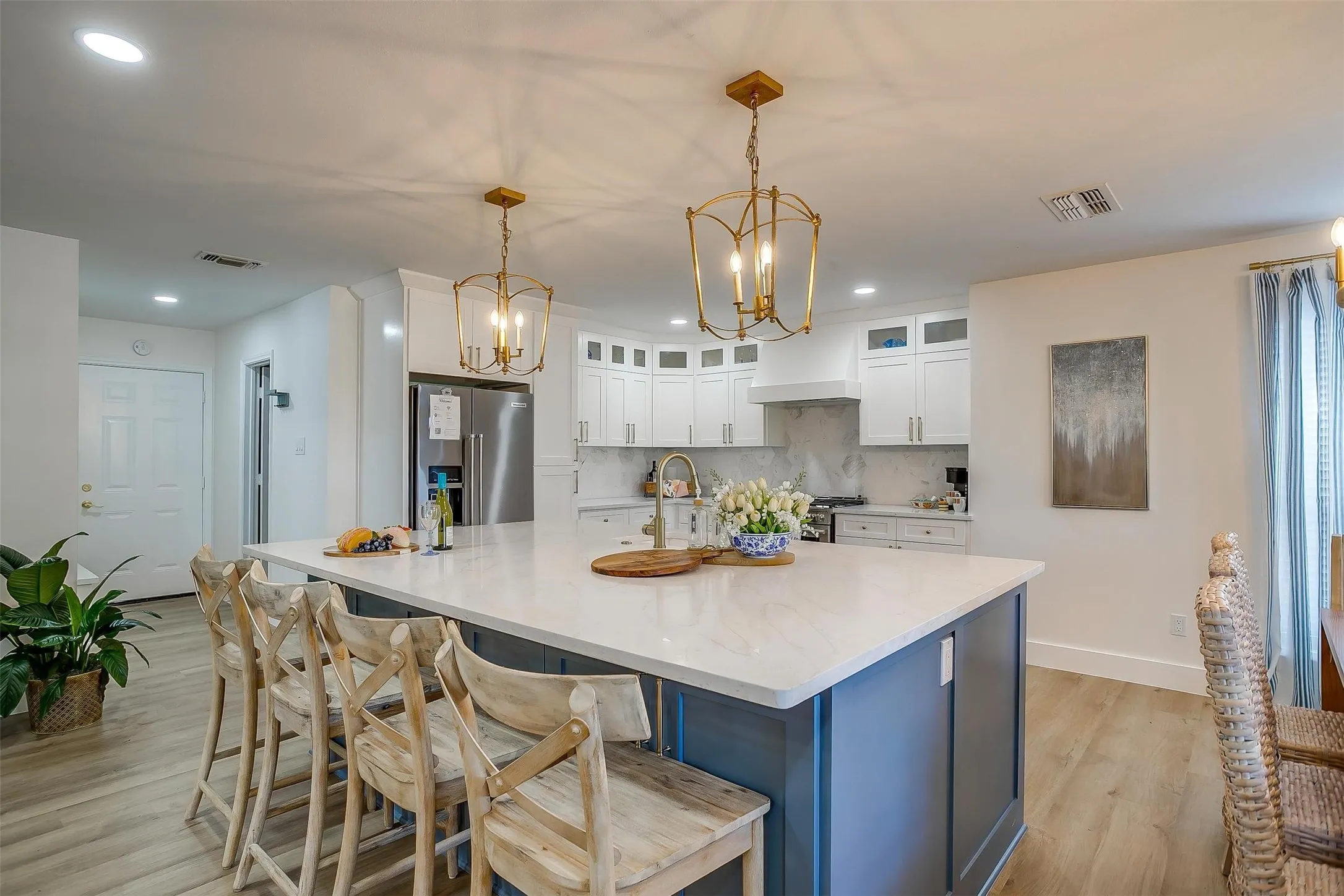 Spacious kitchen featuring a large central island with a light-toned countertop, custom blue cabinetry, and brass lantern-style pendant lighting