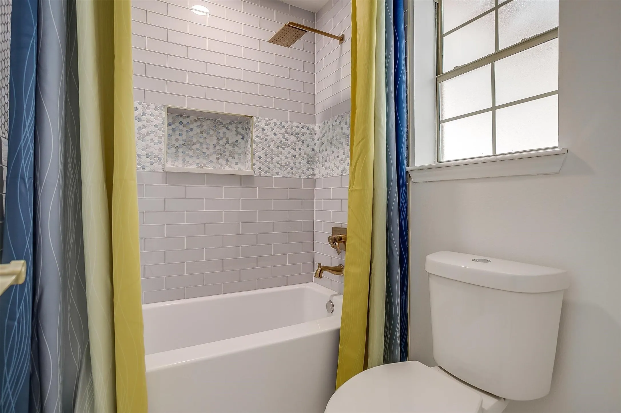 Bathroom featuring a white bathtub, subway tile surround, recessed shower niche, bronze-finish shower fixtures, and a toilet