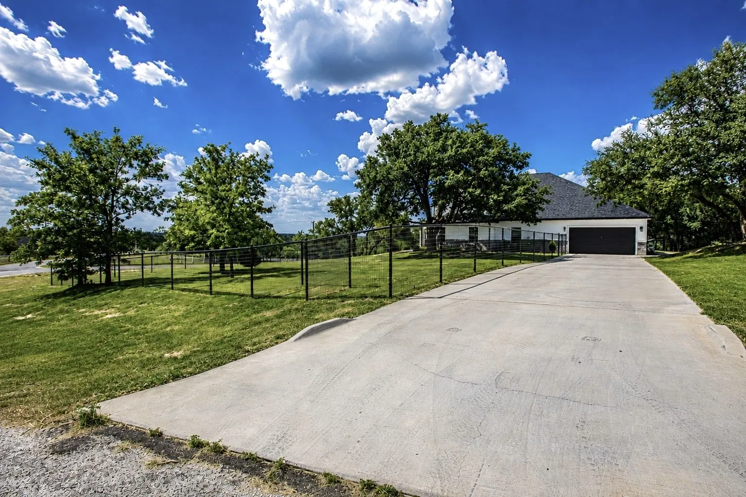 Long concrete driveway leading to a white exterior home with a dark roof and a two-car garage