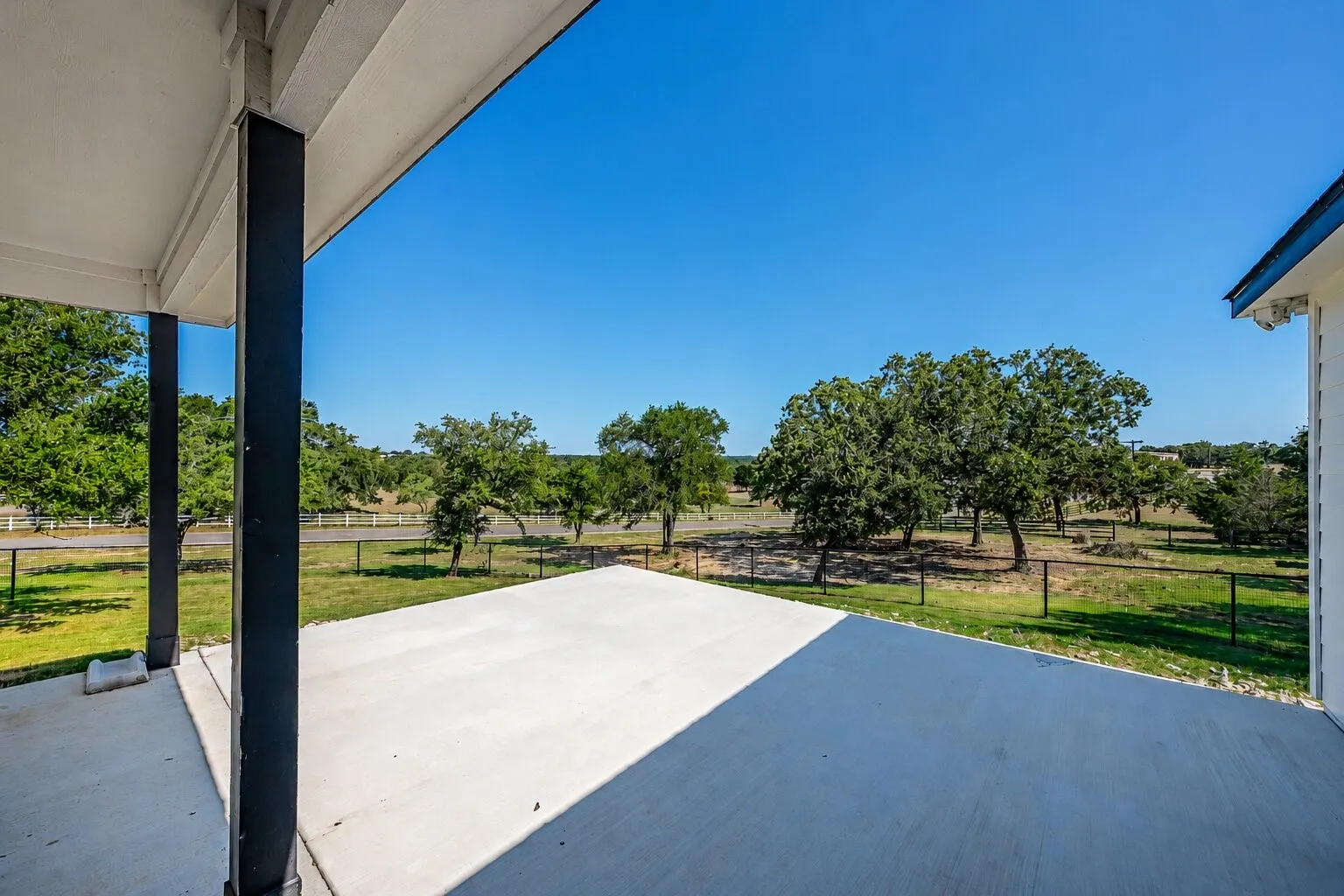 Expansive concrete patio area beneath a covered porch, featuring black support columns and a white ceiling
