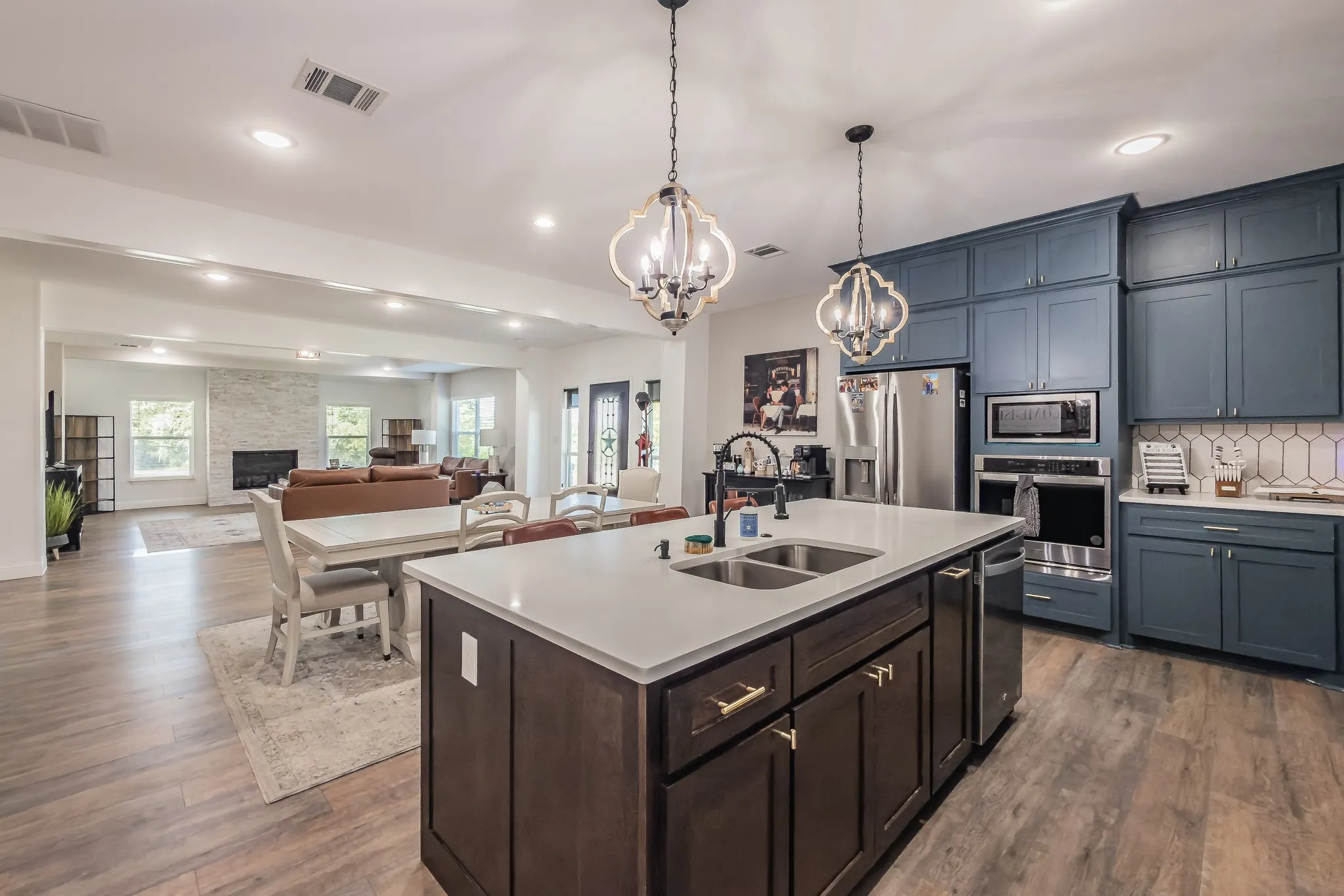 Gourmet kitchen featuring a large central island with an undermount double sink, white quartz countertop, and dark wood cabinetry with gold hardware