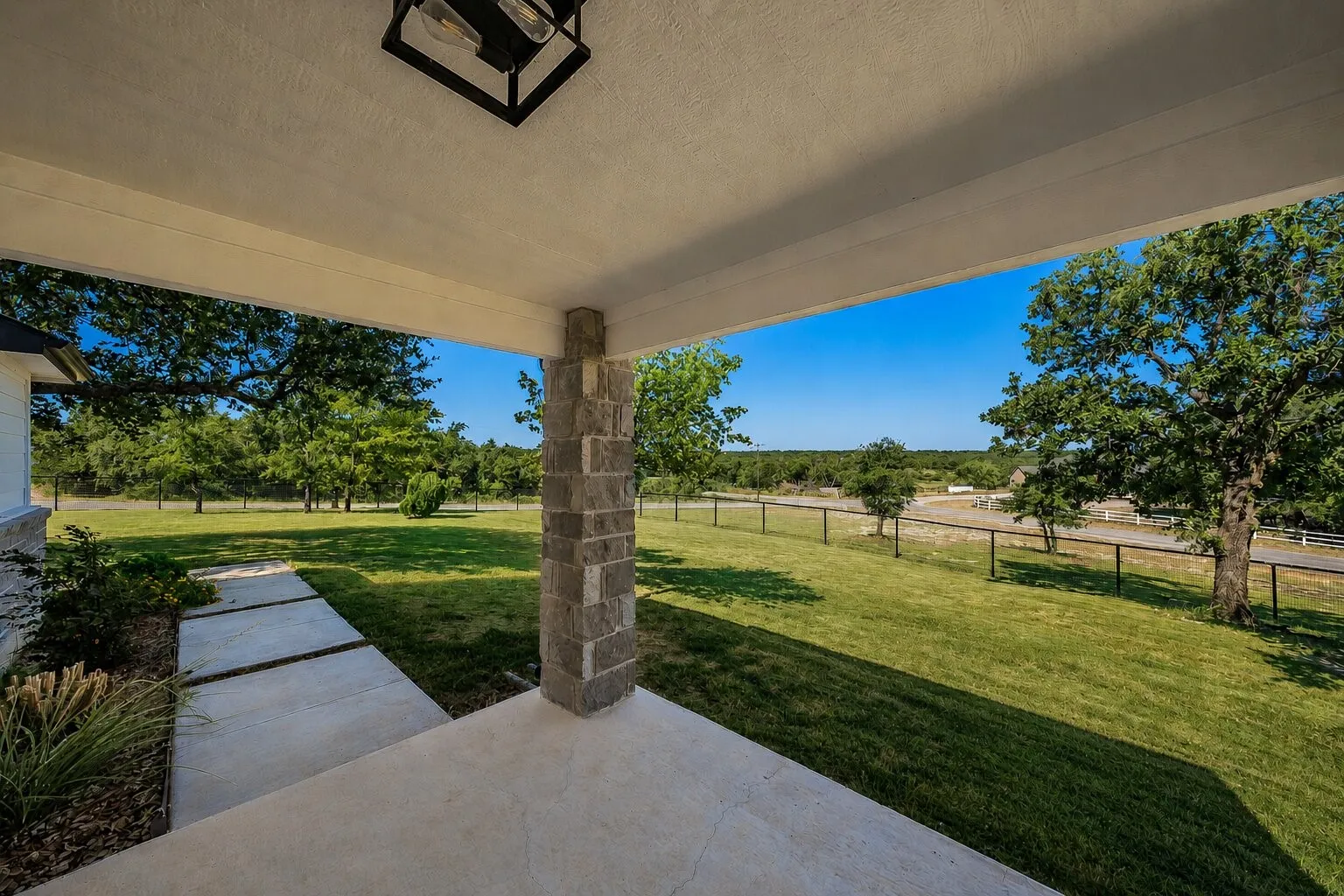 Inviting covered porch with a stone column, concrete flooring, and a contemporary ceiling light fixture