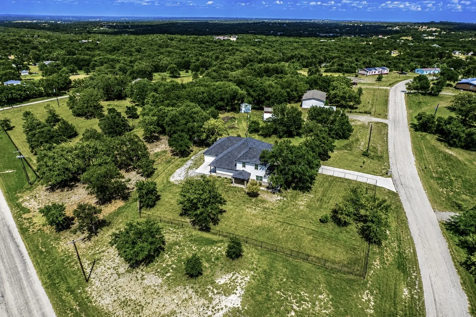 Aerial view showcasing a modern residence with a dark-pitched roof, white siding, and a paved driveway