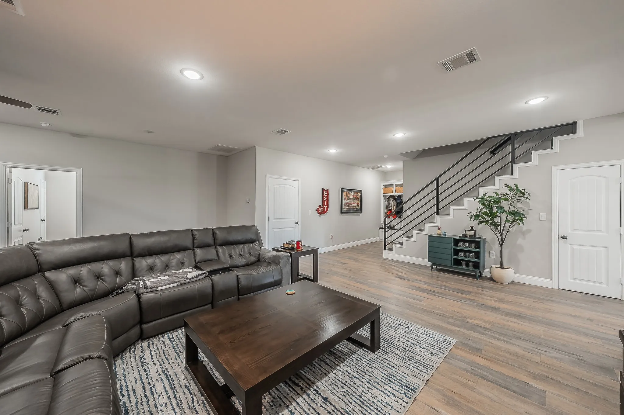 Open concept living area featuring light wood-finish flooring, recessed ceiling lighting, and a modern staircase with black metal railings