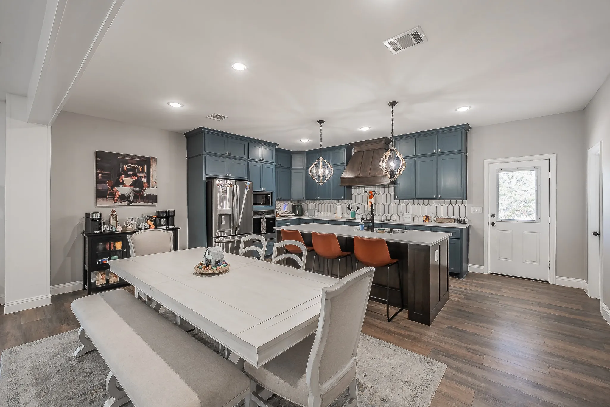 Spacious kitchen featuring deep blue cabinetry, stainless steel appliances, a large island with seating, and wood-finish flooring