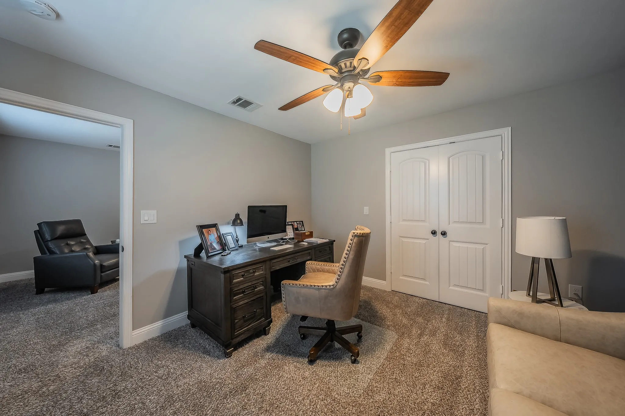 Well-appointed room featuring grey wall paint, plush carpet flooring, a ceiling fan with light fixture, and white double doors with black hardware