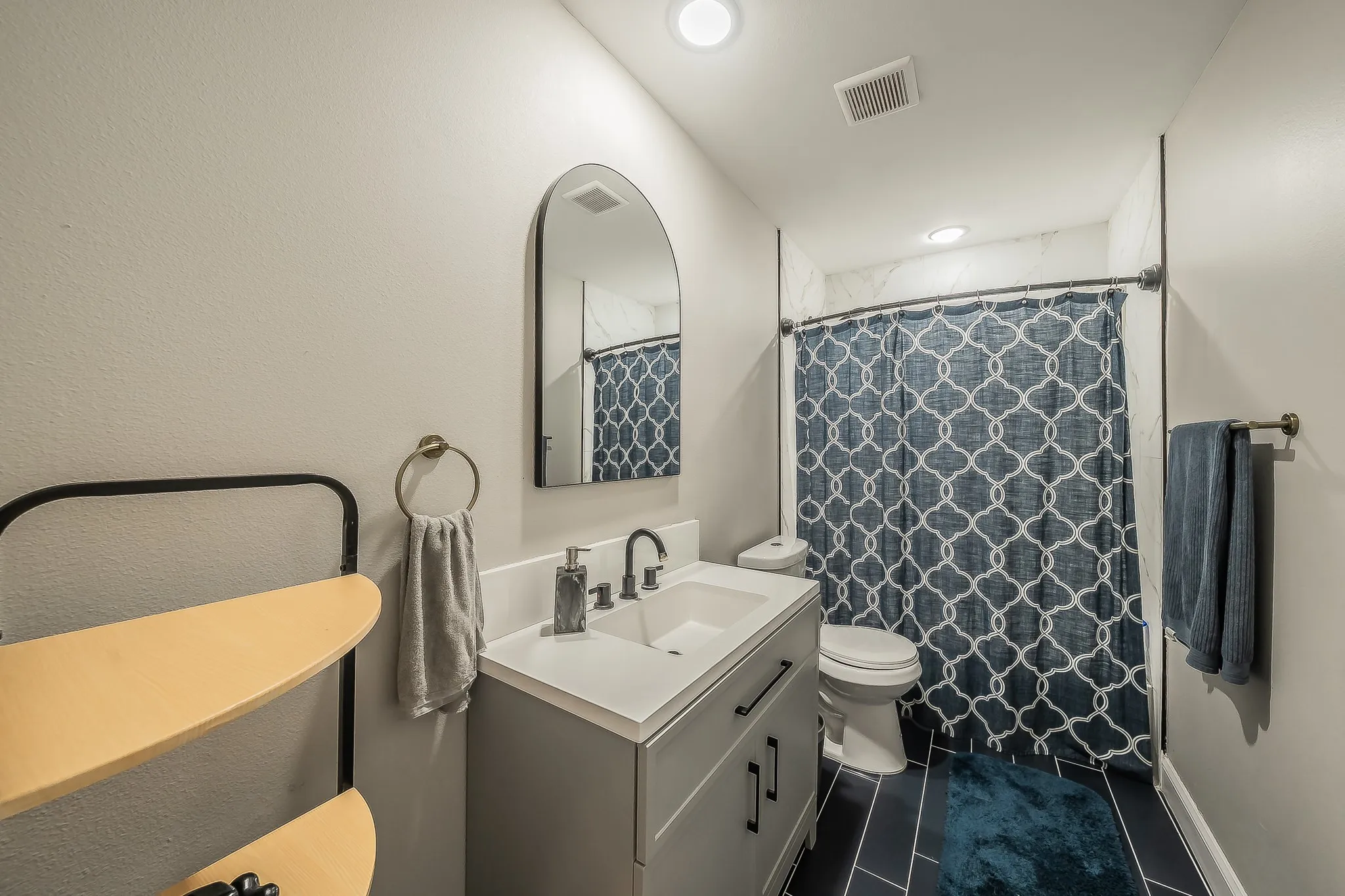 Bathroom featuring a white integrated sink vanity with dark hardware, a framed arched mirror, and white tiled walls surrounding the shower area