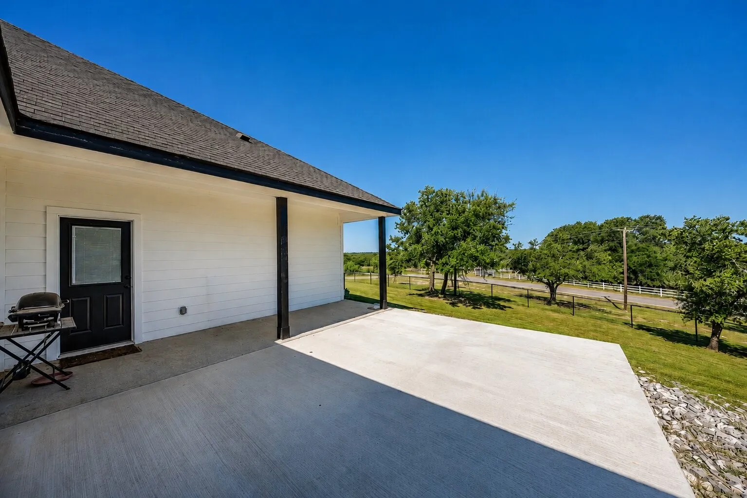 Expansive concrete patio with covered area, white horizontal siding, dark asphalt shingle roof, and black trim details