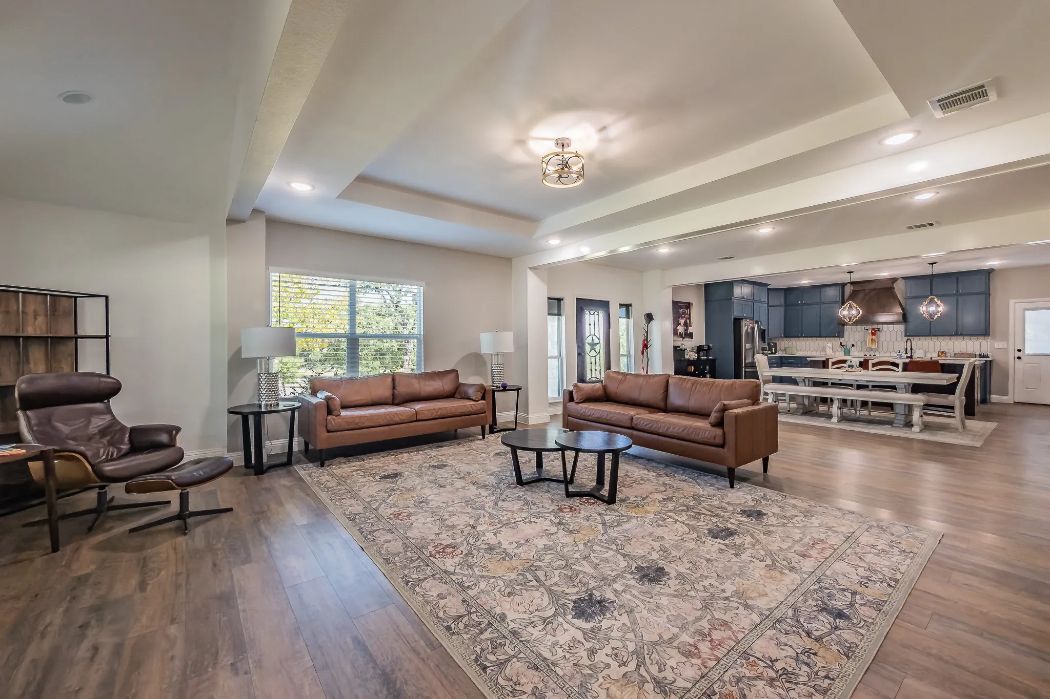 Open-concept living area with wood-finish flooring, recessed lighting, tray ceiling, and a prominent window