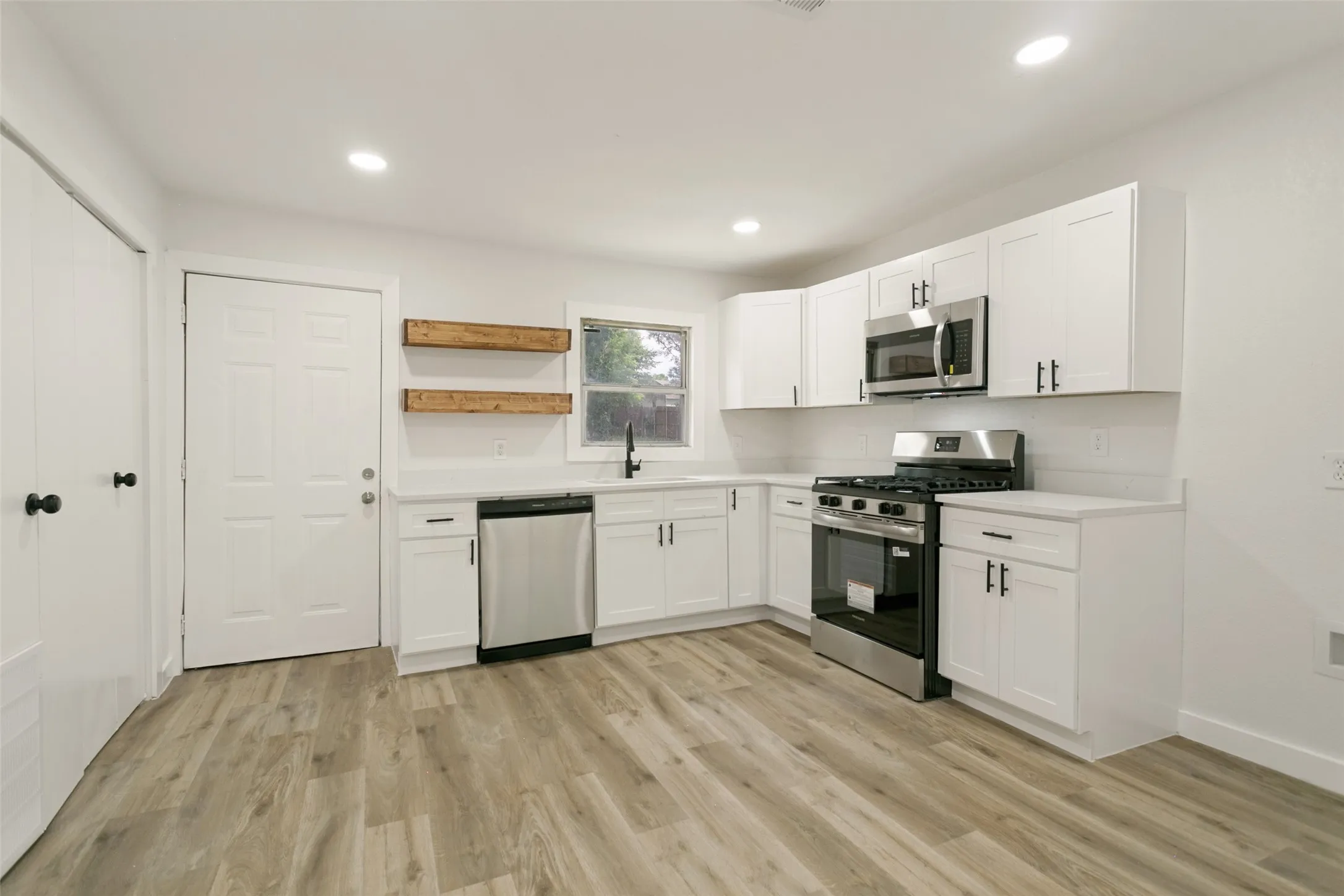 Modern kitchen featuring white cabinetry, stainless steel appliances, light-toned wood-finish flooring, a white subway tile backsplash, and recessed lighting