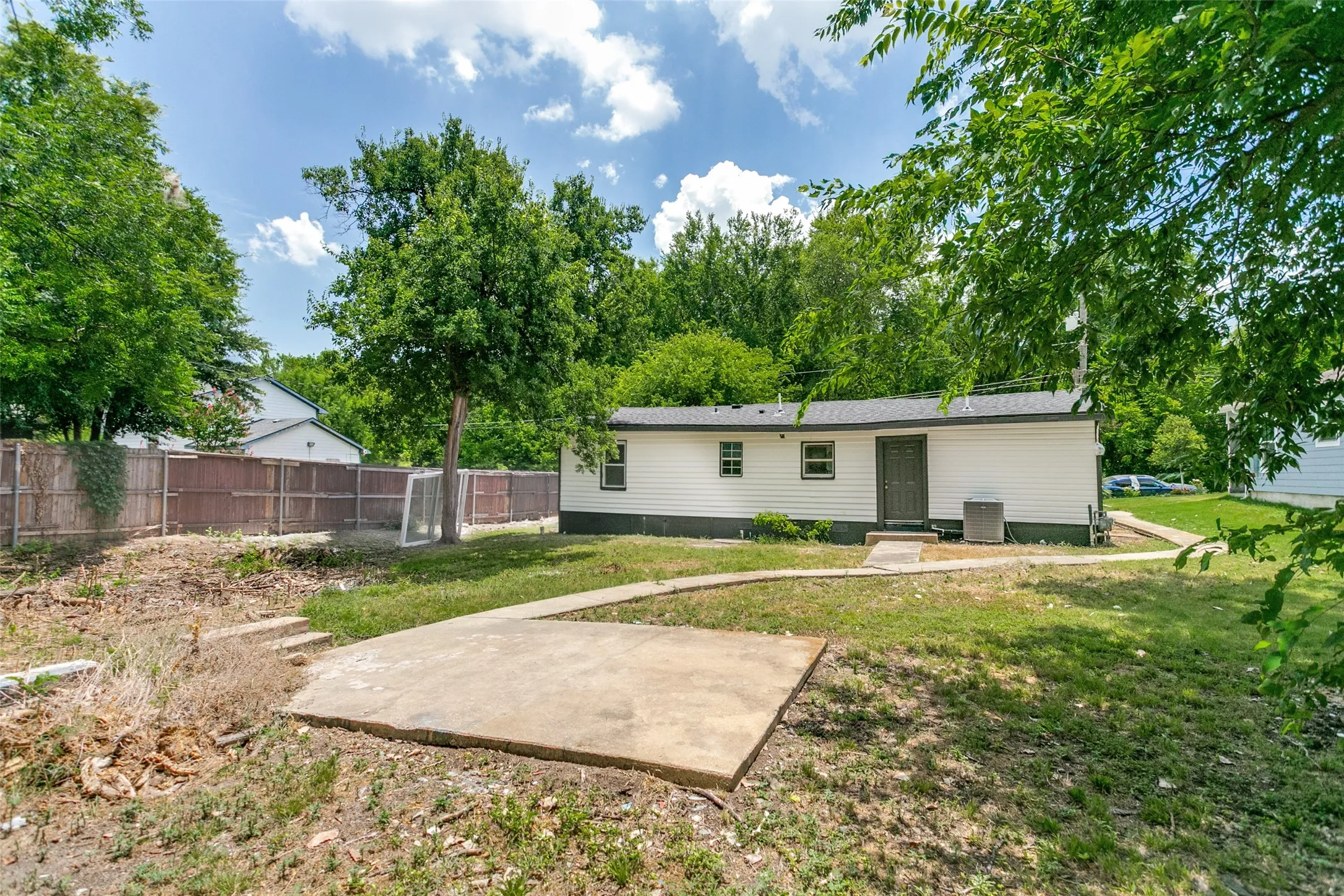 Backyard featuring a concrete patio, established trees, and a wooden fence