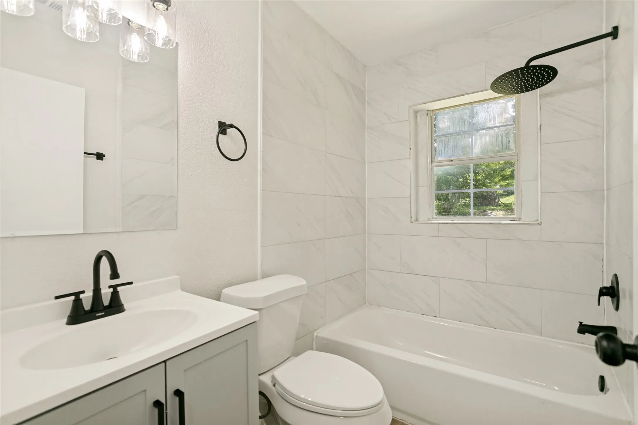 Bathroom featuring a white bathtub with a rainfall showerhead, white subway tile surround, and a window