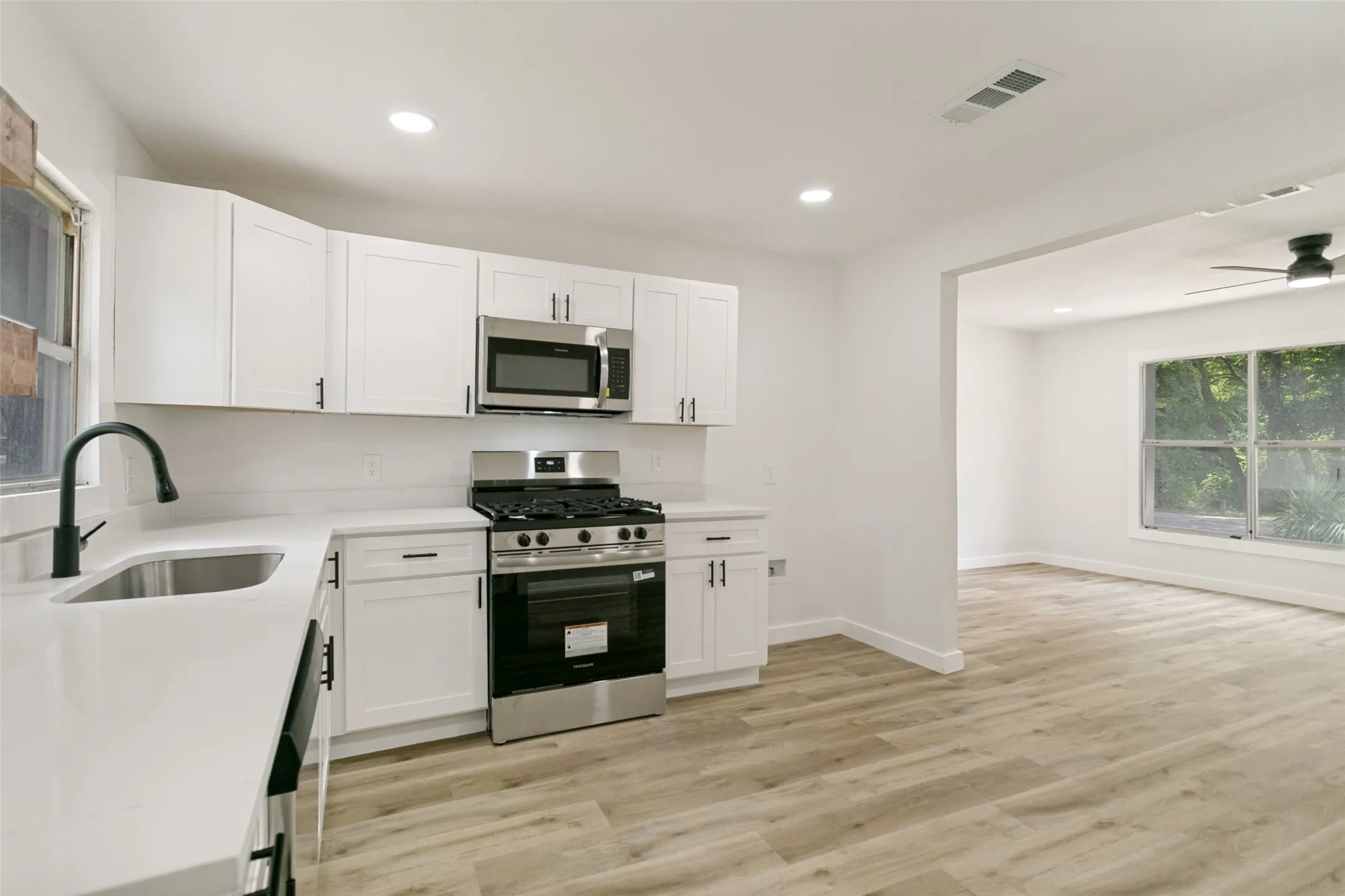 Modern kitchen featuring white shaker cabinetry, stainless steel appliances, light-toned wood-finish flooring, and a matte black gooseneck faucet