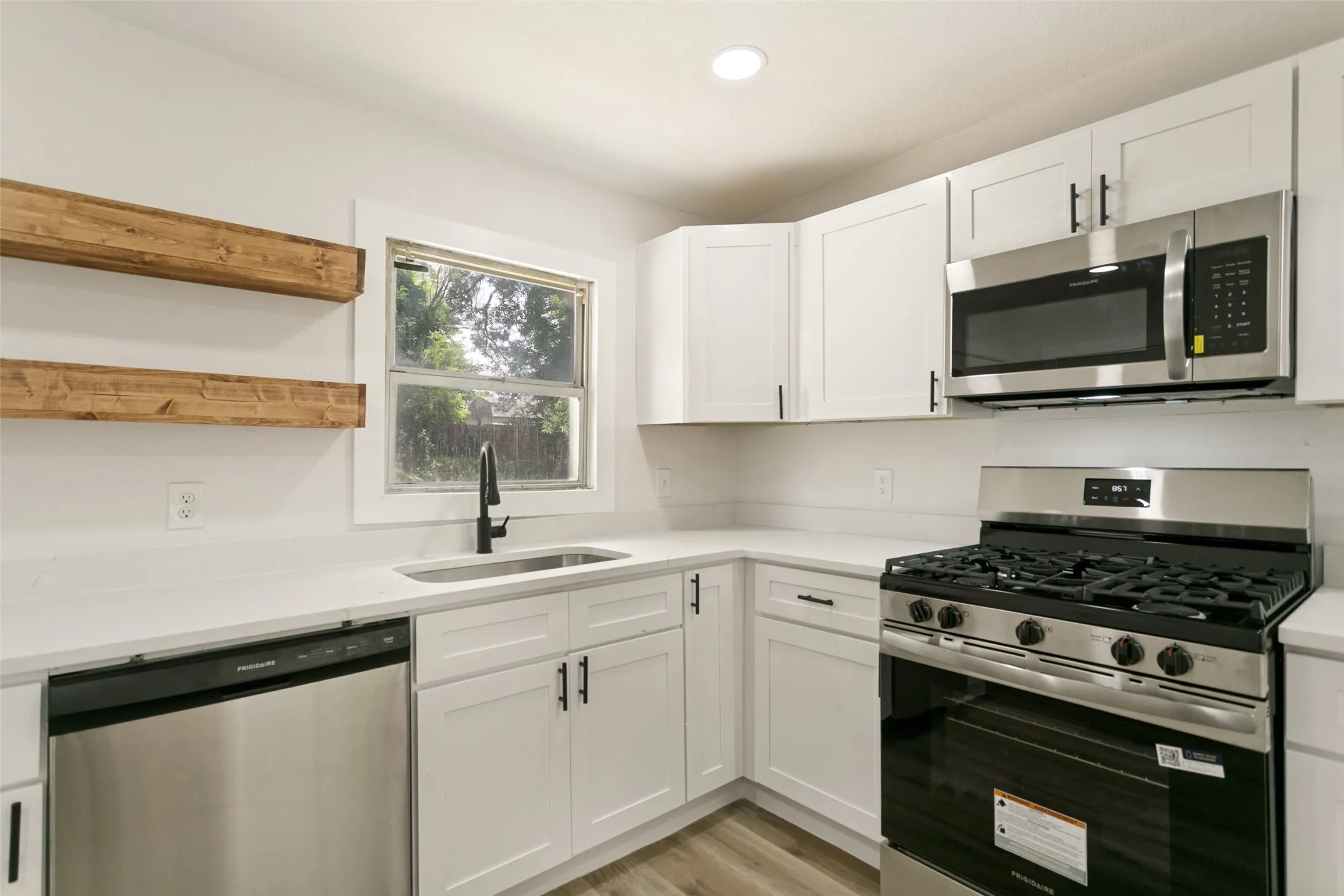 Modern kitchen featuring white shaker cabinetry, stainless steel appliances, a stainless steel sink with a matte black faucet, light countertops, and wood-finish flooring