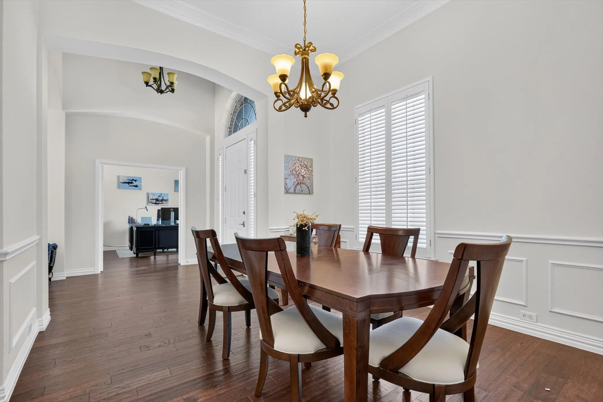 Formal dining space featuring wood-finish flooring, wainscoting, crown molding, and a decorative chandelier