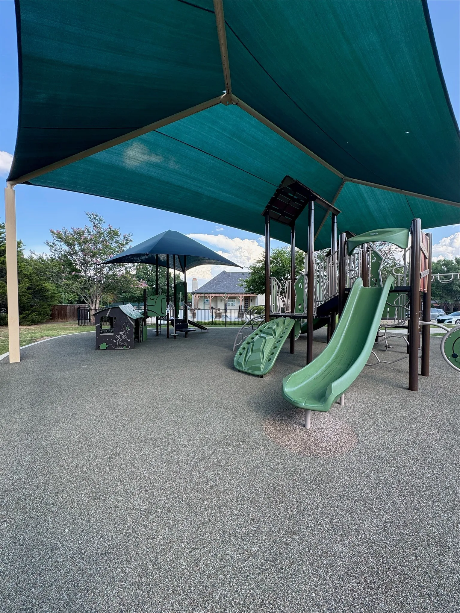 Community playground featuring a large shade canopy, rubberized surface, multiple slides, and play structures