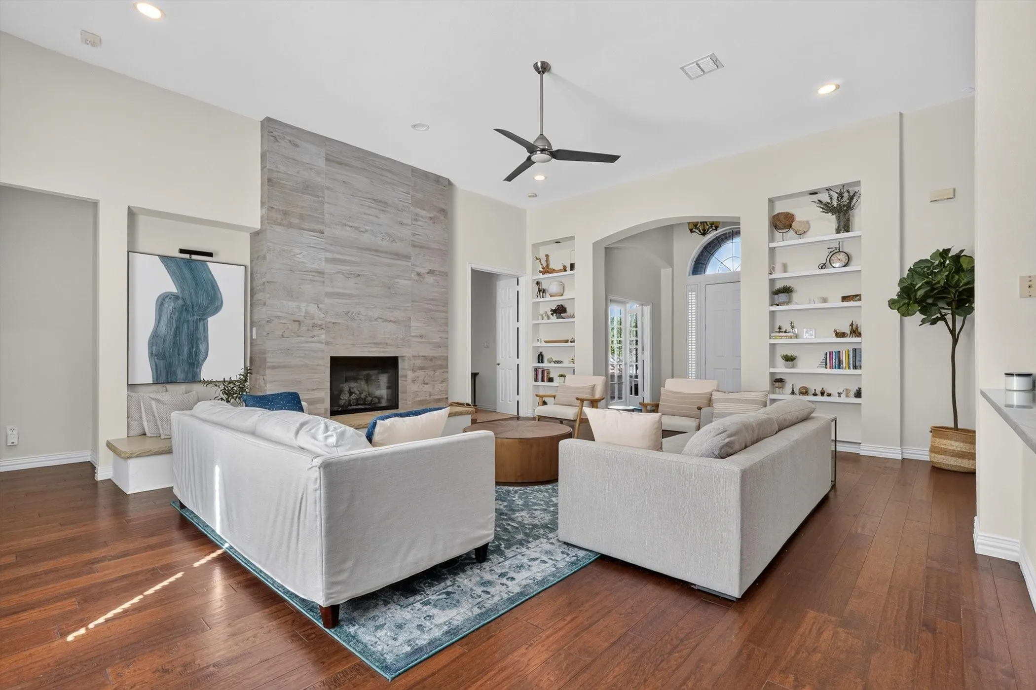 Spacious living area featuring rich wood-finish flooring, a contemporary fireplace with a full-height stone-look surround, and vaulted ceilings