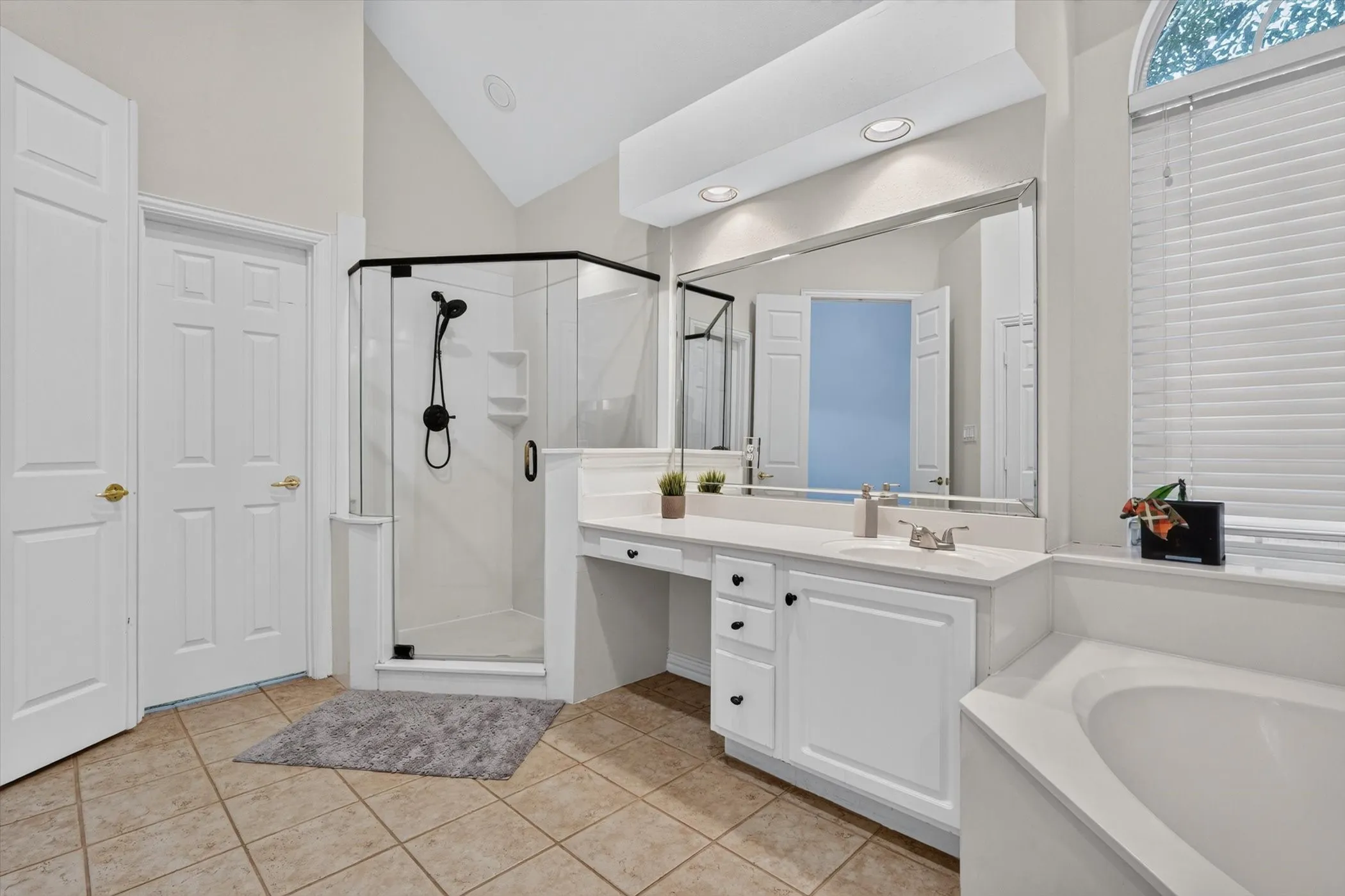 Bathroom featuring a corner glass-enclosed shower with black fixtures, a built-in soaking tub, and a dual vanity with ample countertop space and storage
