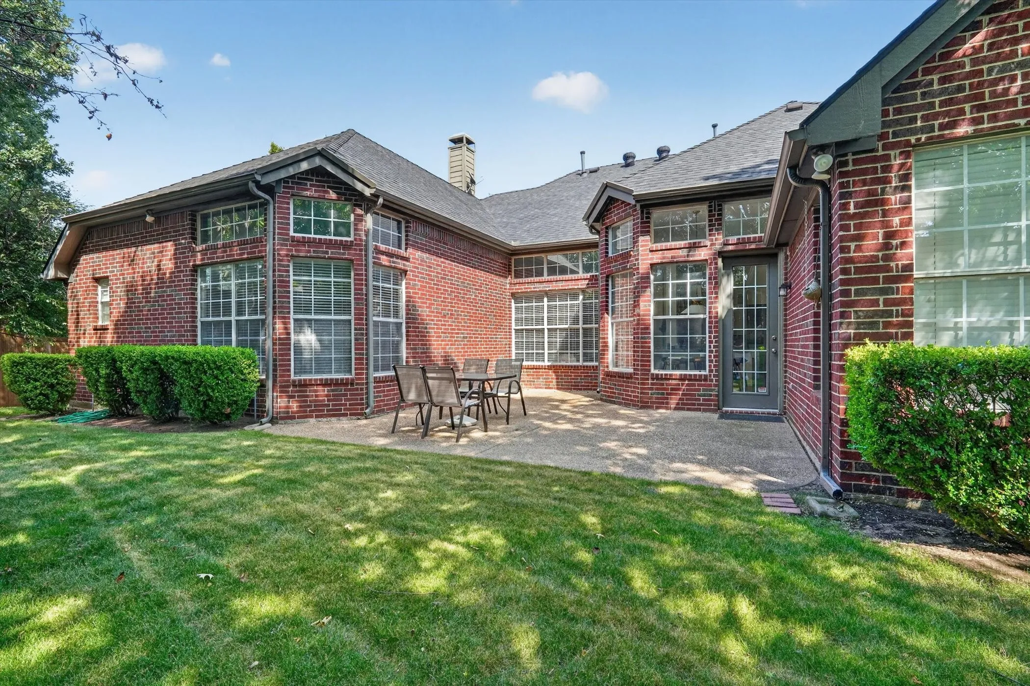 Brick exterior featuring multiple bay windows, a paved patio, and a manicured lawn