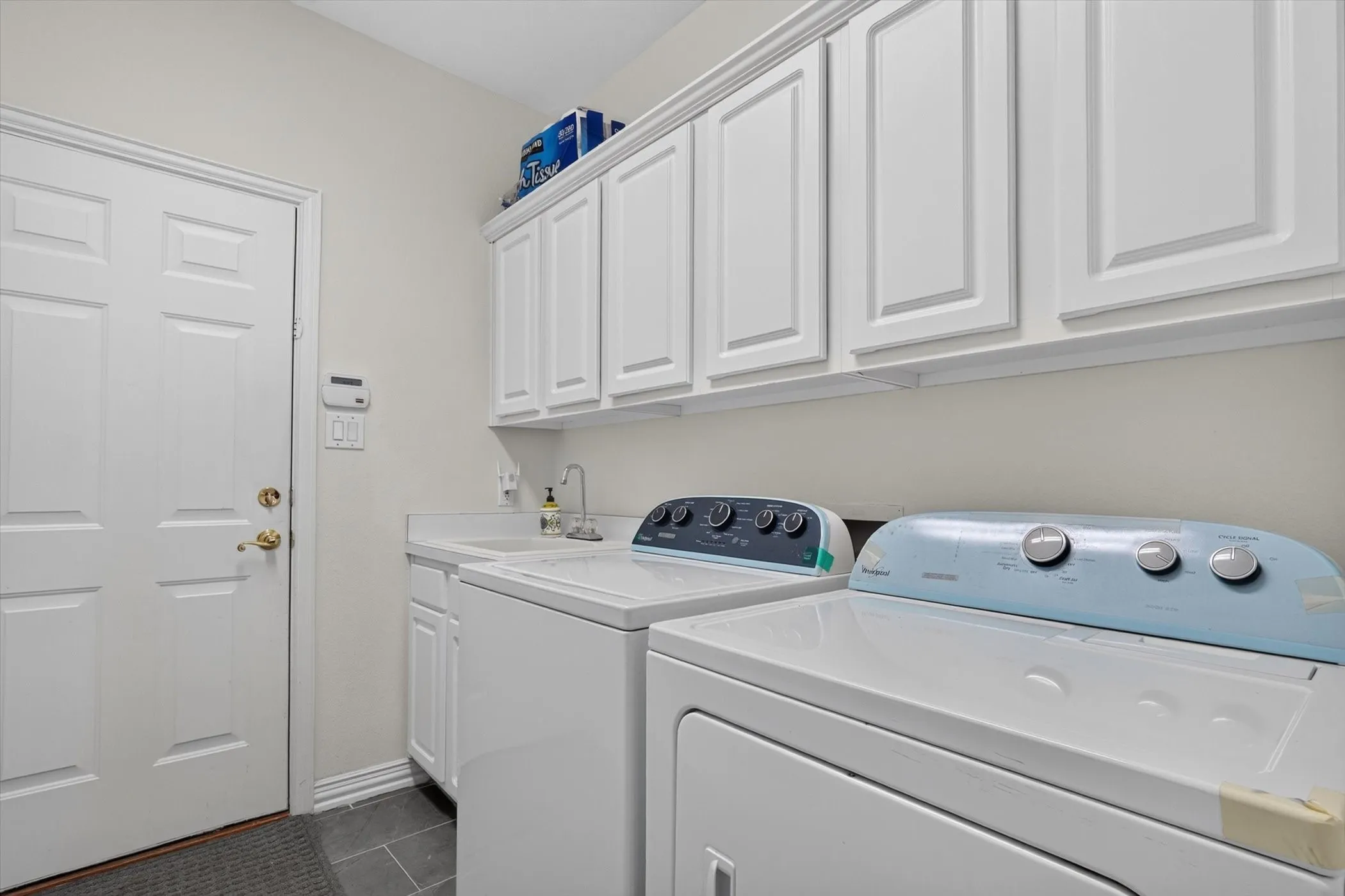 Utility room featuring white cabinetry, a built-in sink with a gooseneck faucet, and dark tile flooring