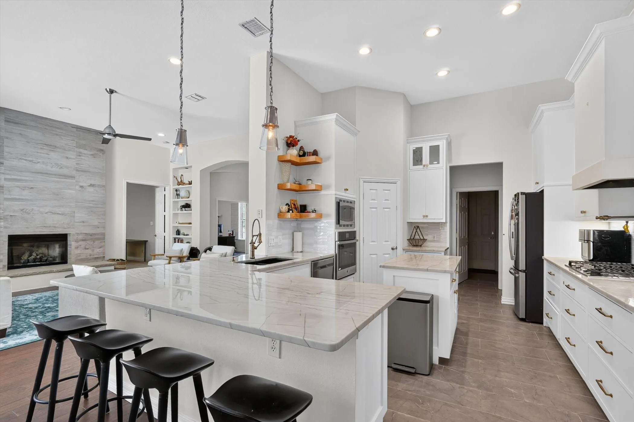 Open-concept kitchen featuring an expansive island with seating, stainless steel appliances, white cabinetry, and light-toned countertops