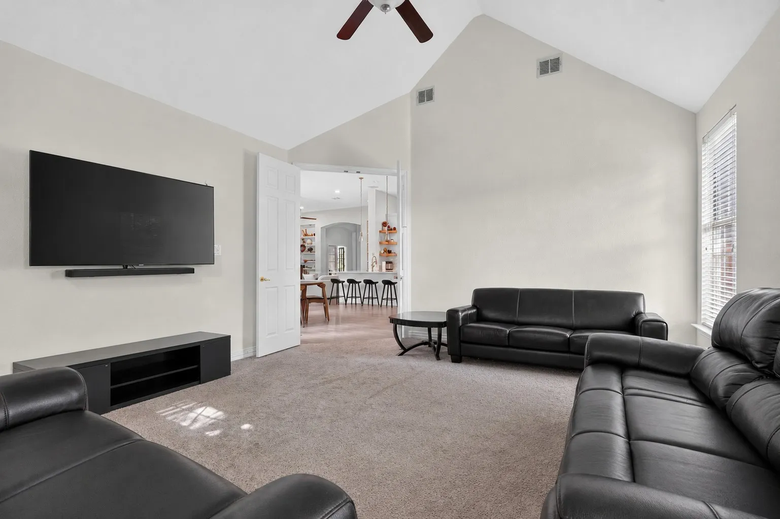Spacious living area featuring vaulted ceilings, neutral wall tones, and carpet flooring