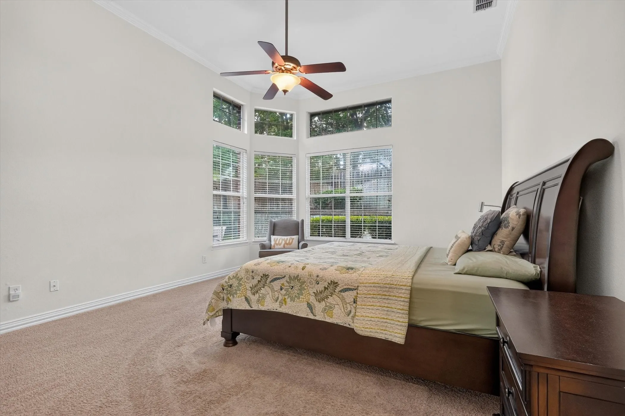 Vaulted ceiling bedroom with corner window array, crown molding, and a ceiling fan with integrated lighting