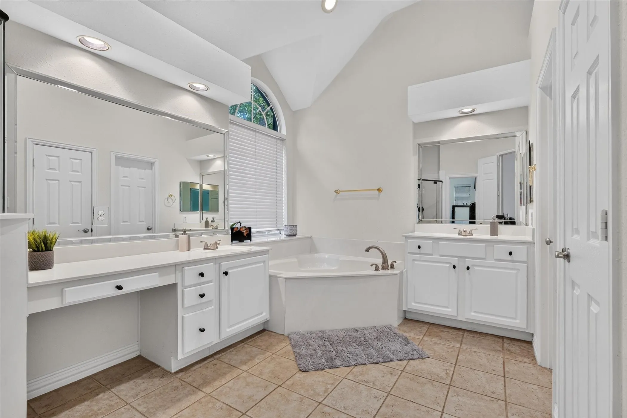Bathroom featuring a built-in garden tub, dual vanities with white cabinetry, and large format tile flooring