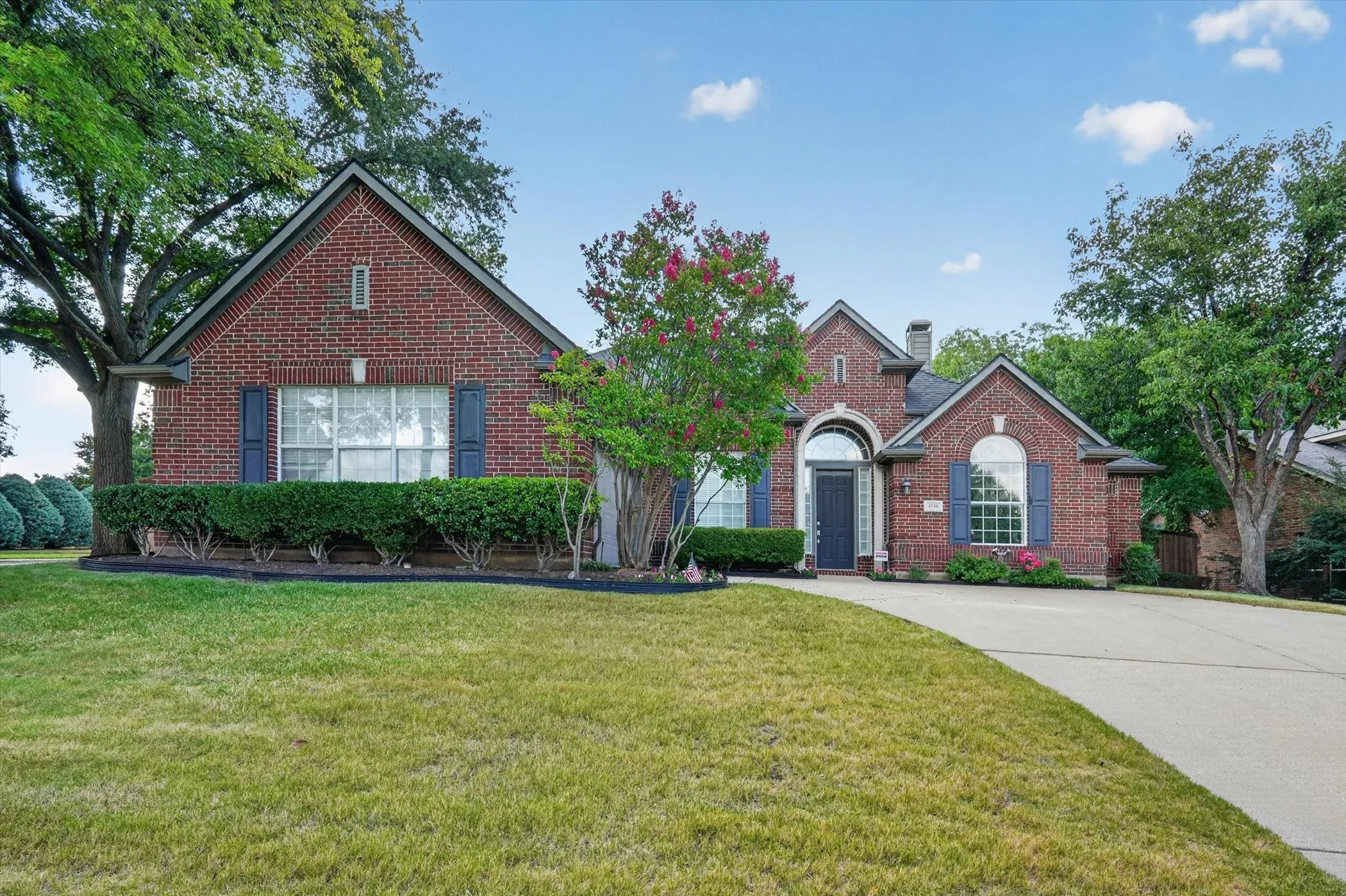 Brick facade residence featuring a front gabled roofline, arched entry, decorative window shutters, and a concrete driveway