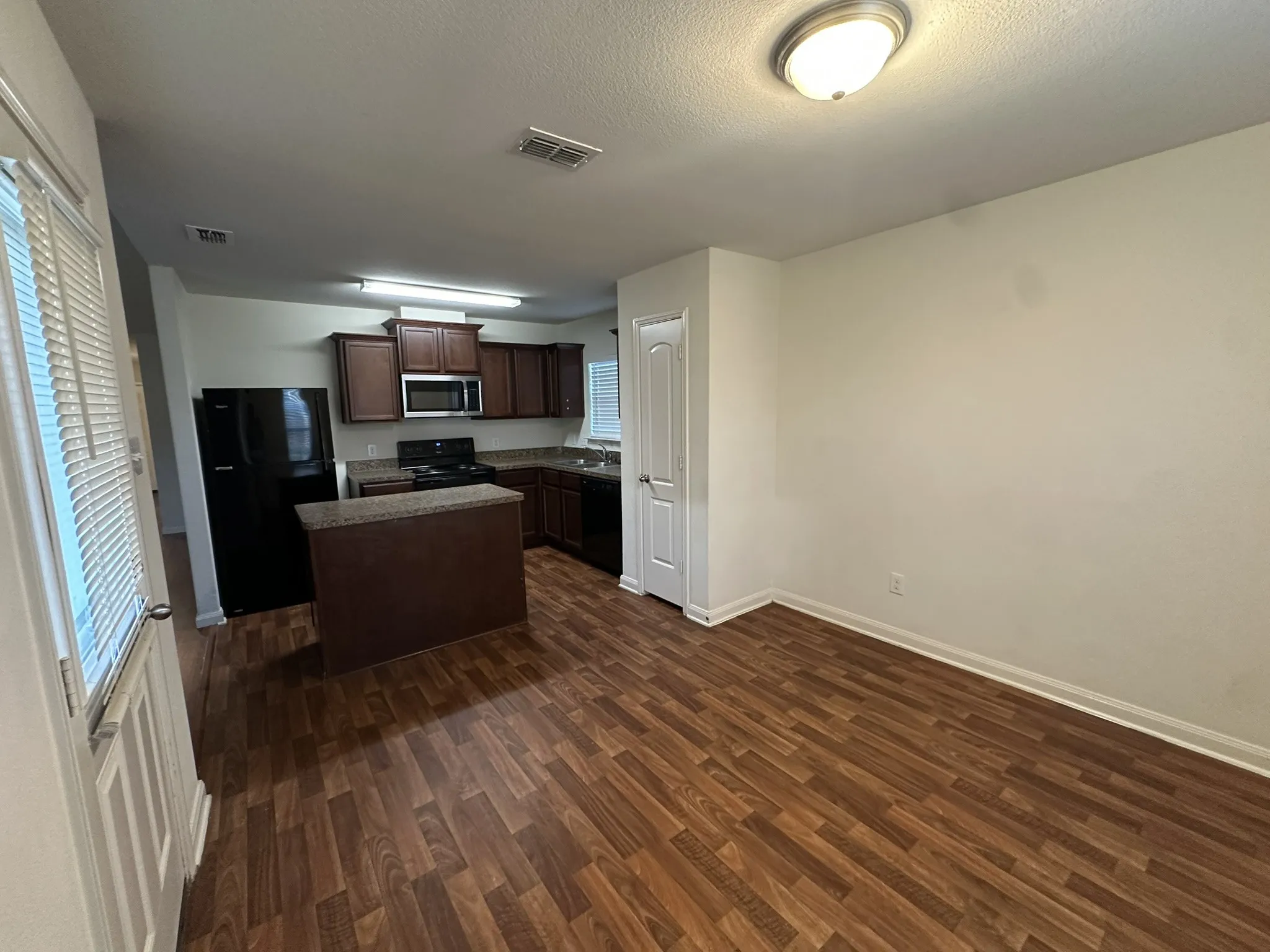 Kitchen and dining area featuring wood-finish flooring, dark wood cabinetry, granite-style countertops, and a full suite of black appliances